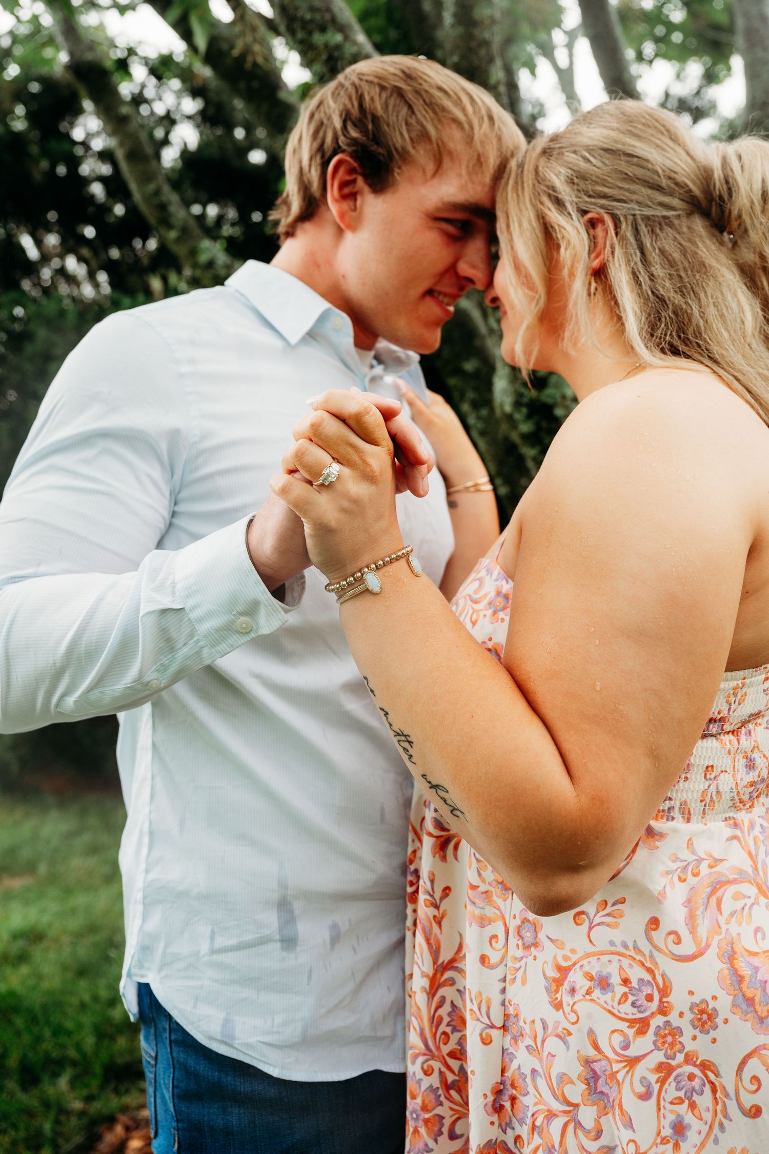 Couple sharing a romantic moment, holding hands and touching foreheads in a lush green garden setting.