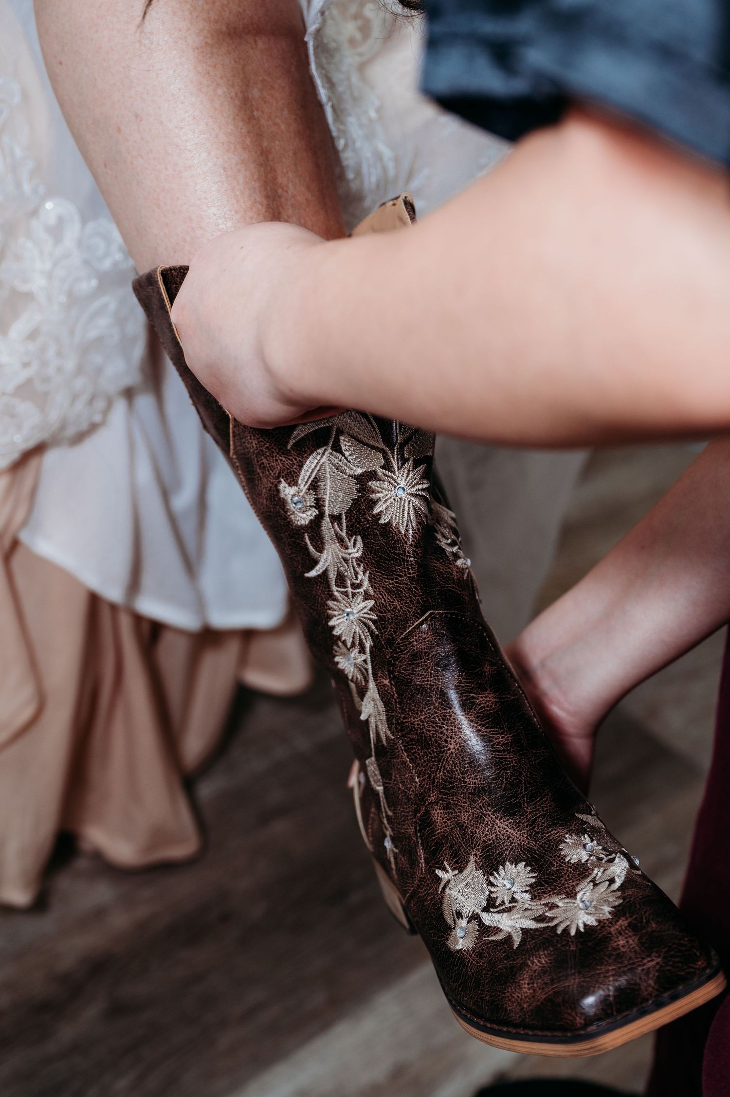 Close-up of embroidered brown leather cowboy boot with white floral design being worn with a light-colored dress.
