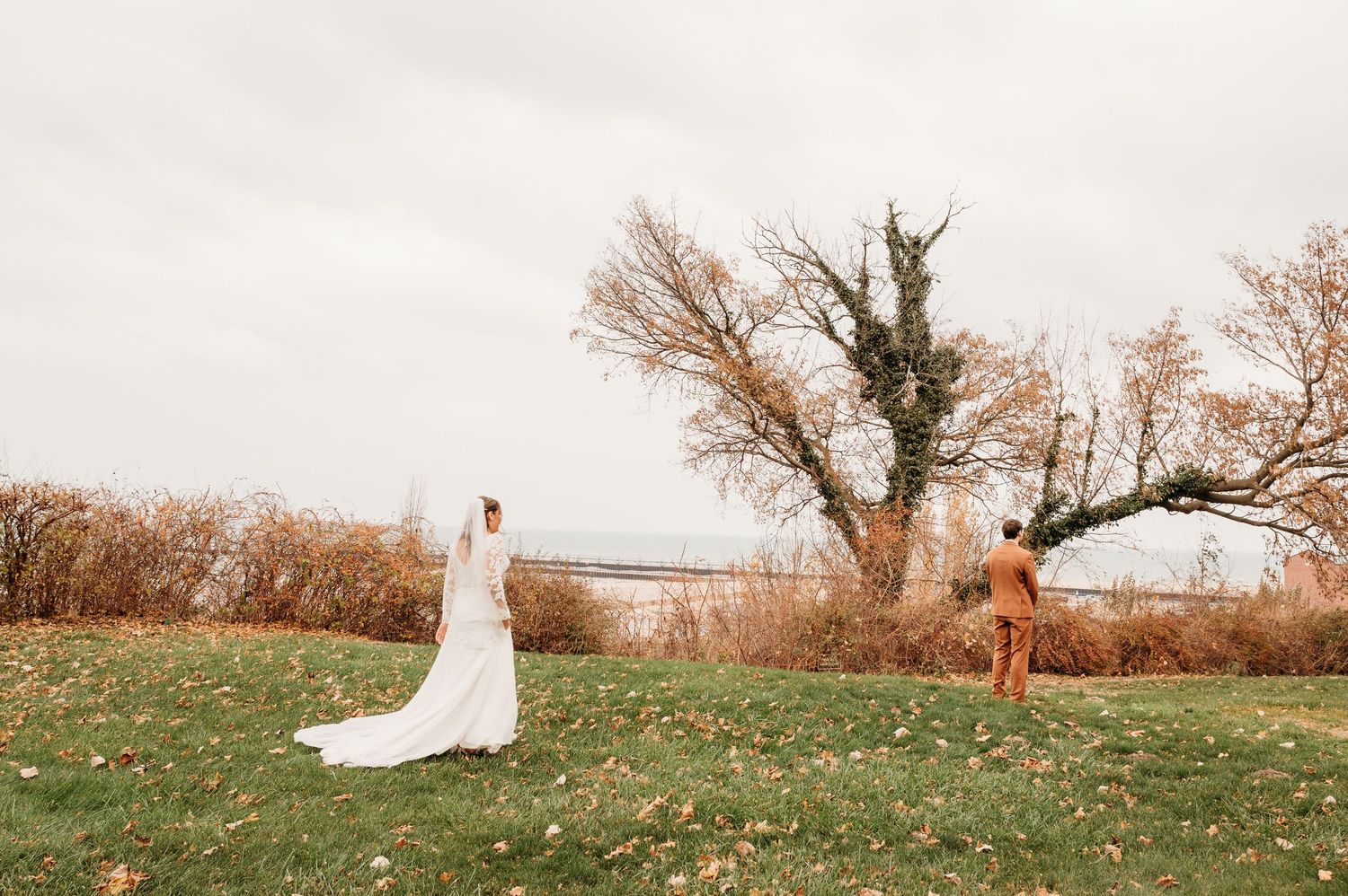 A flowing white wedding dress trails behind someone walking through an autumn field at sunset.