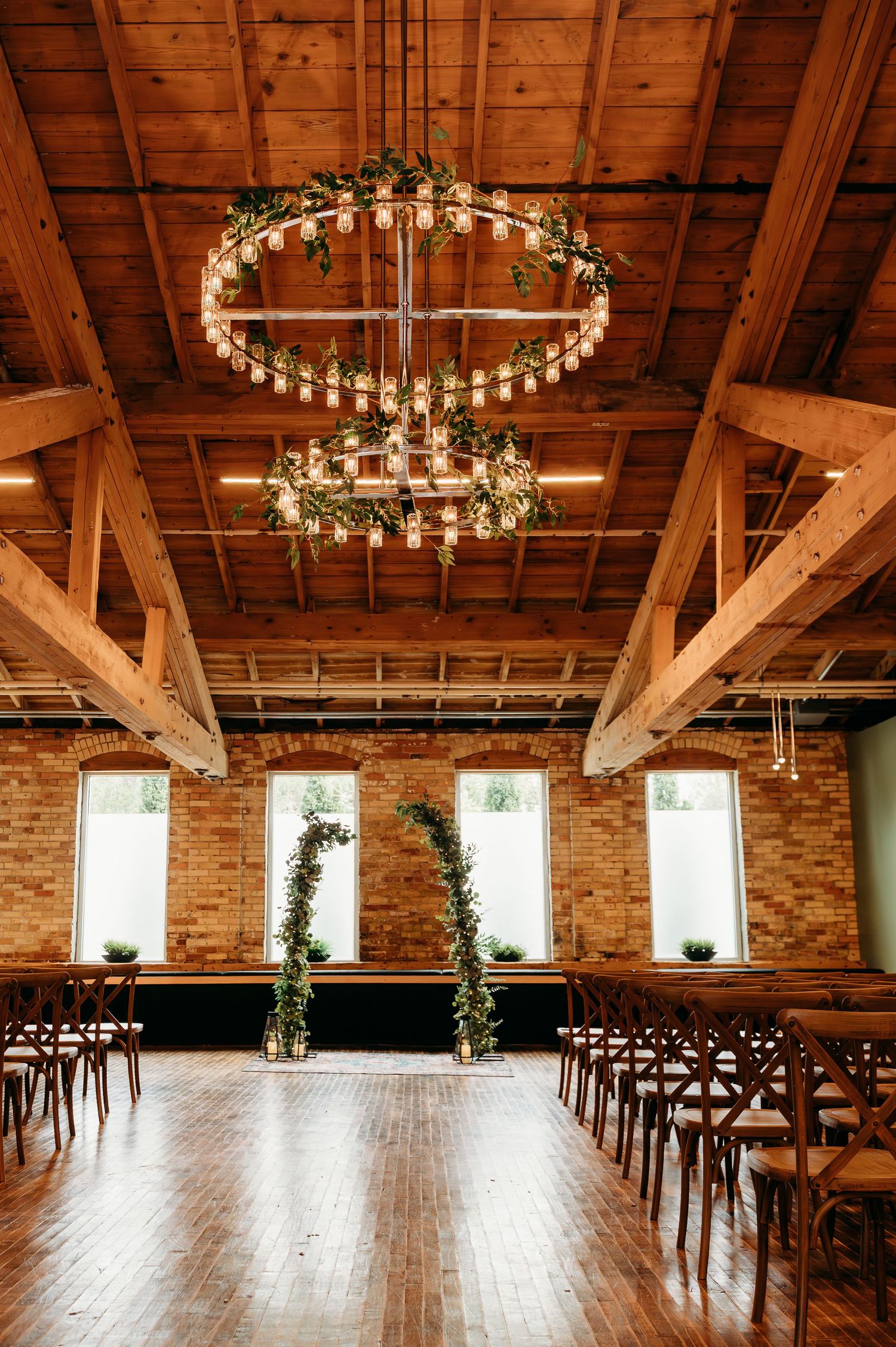 Rustic barn wedding venue with exposed wooden beams, circular chandeliers, and rows of chairs set up for a ceremony.