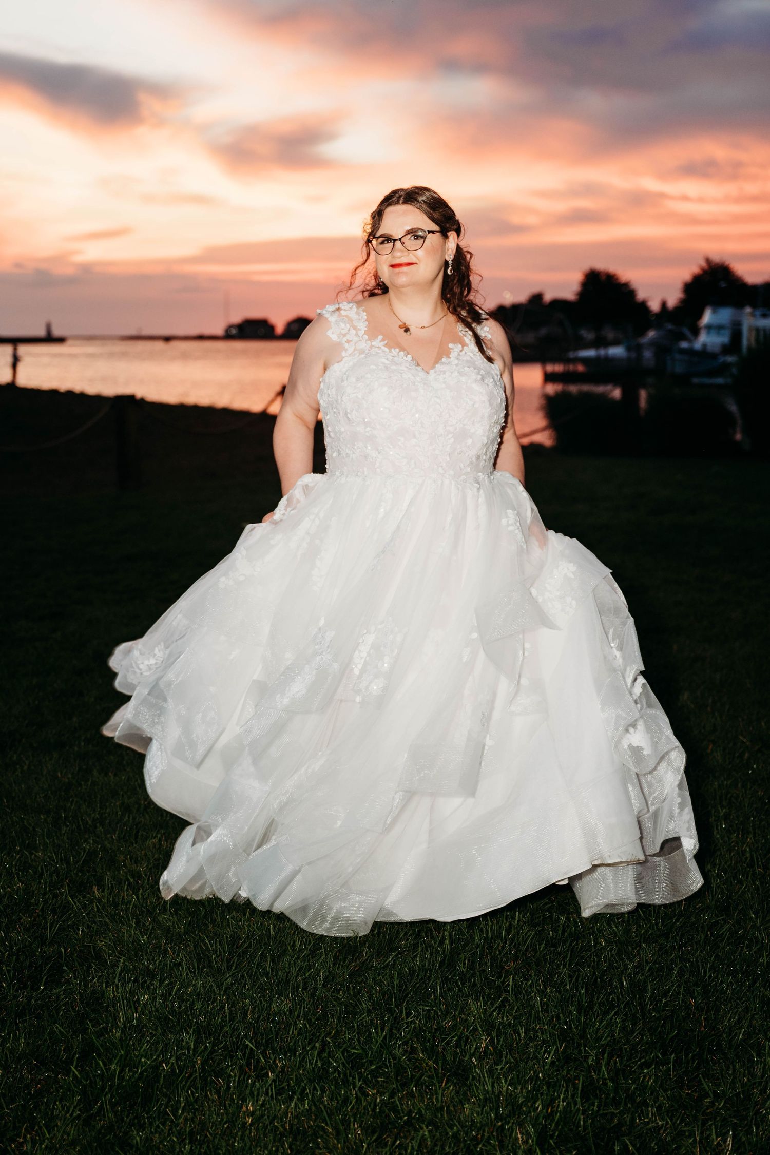 Flowing white wedding dress skirt photographed against a dramatic sunset sky in an outdoor field.