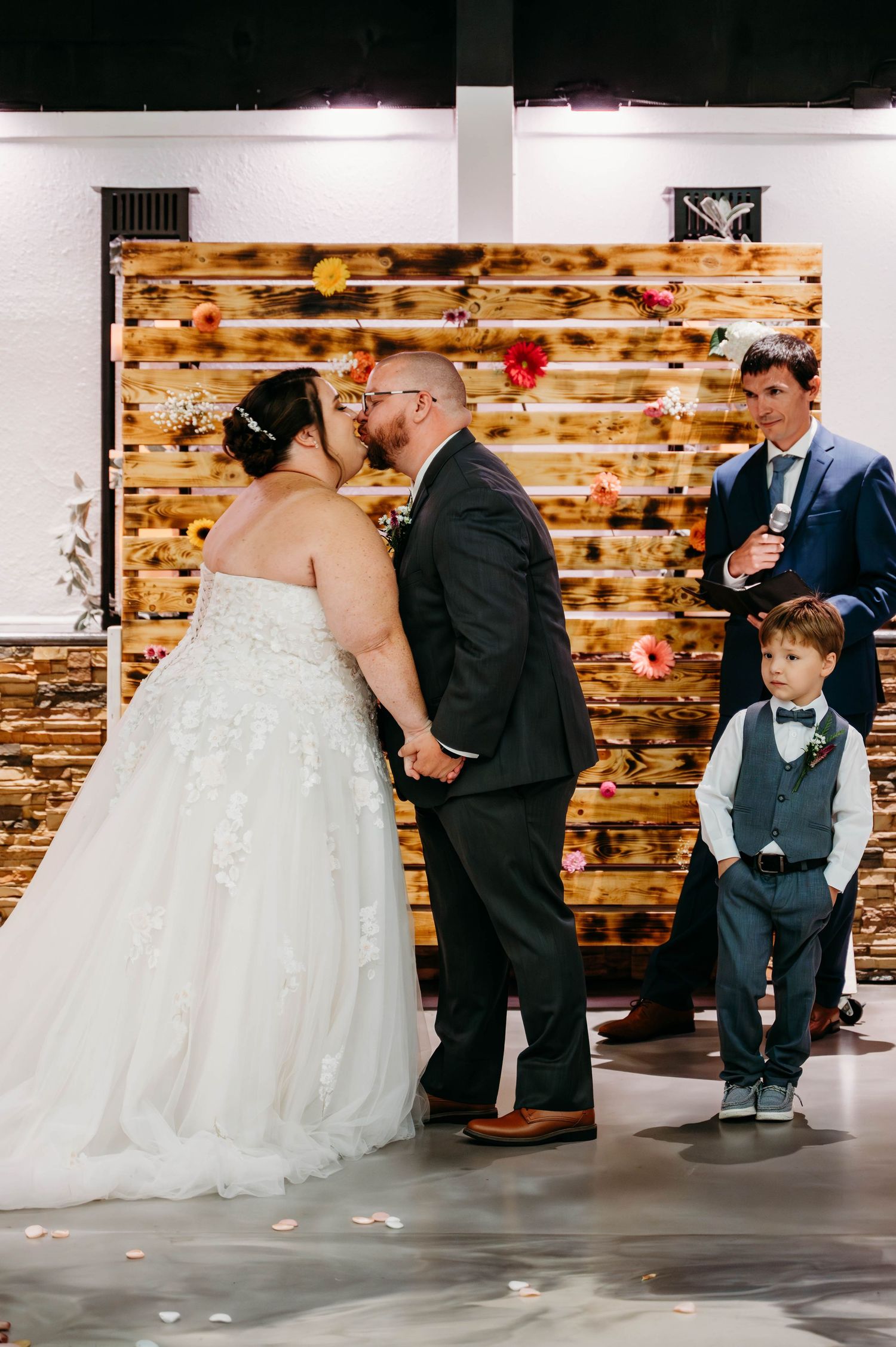 A sweet sequence of wedding photos showing a couple sharing their first kiss while a young ring bearer reacts with playful disgust.