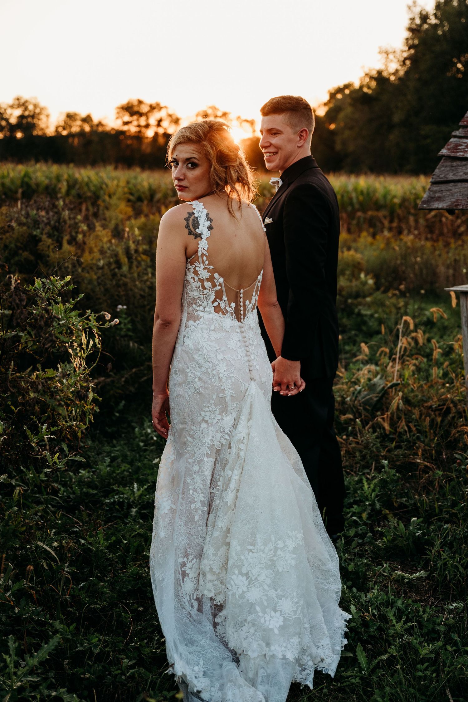 A couple in wedding attire walks through a wildflower field at sunset during their outdoor wedding photoshoot.