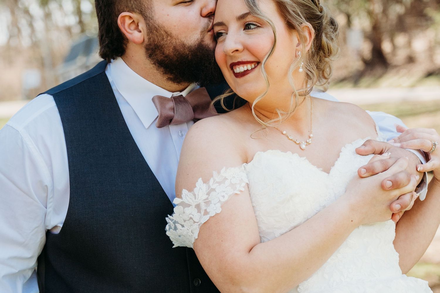 A tender moment between a bride and groom at an outdoor wedding venue during a bright sunny day.
