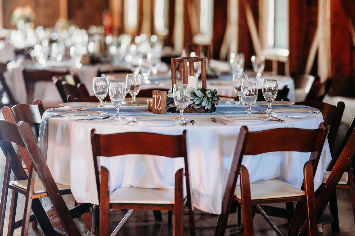 Elegant wedding reception venue with white tablecloths and dark wooden chairs in a rustic restaurant setting.