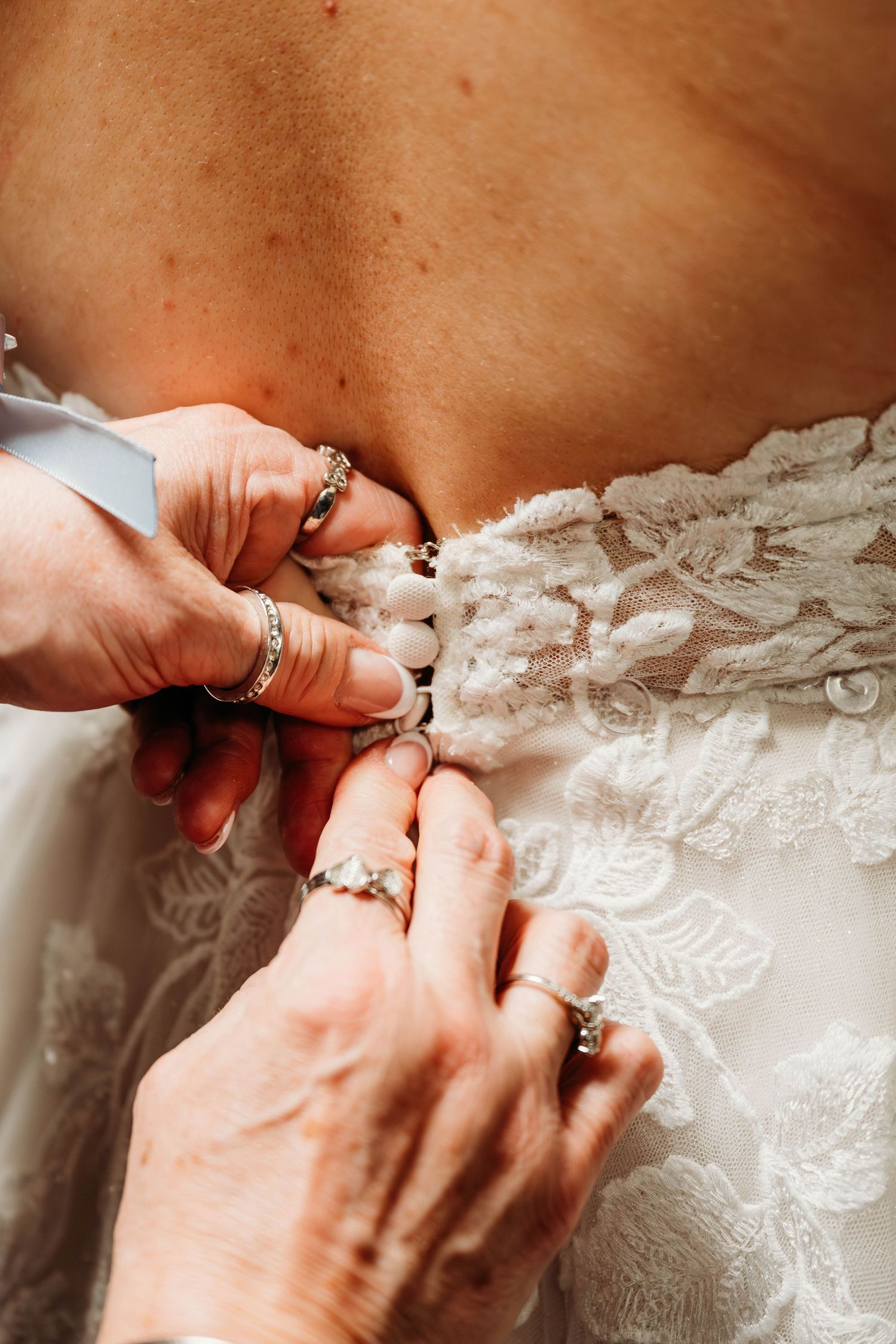 Close-up of delicate lace detail being fastened on a white wedding dress.