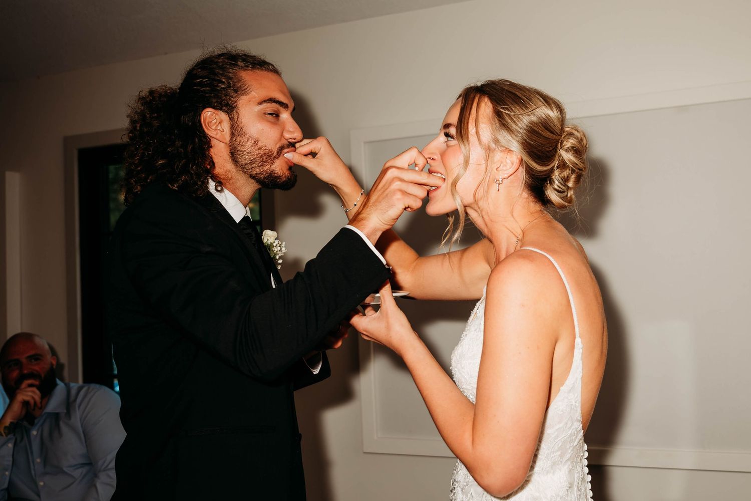 Bride and groom feeding each other wedding cake during reception celebration.