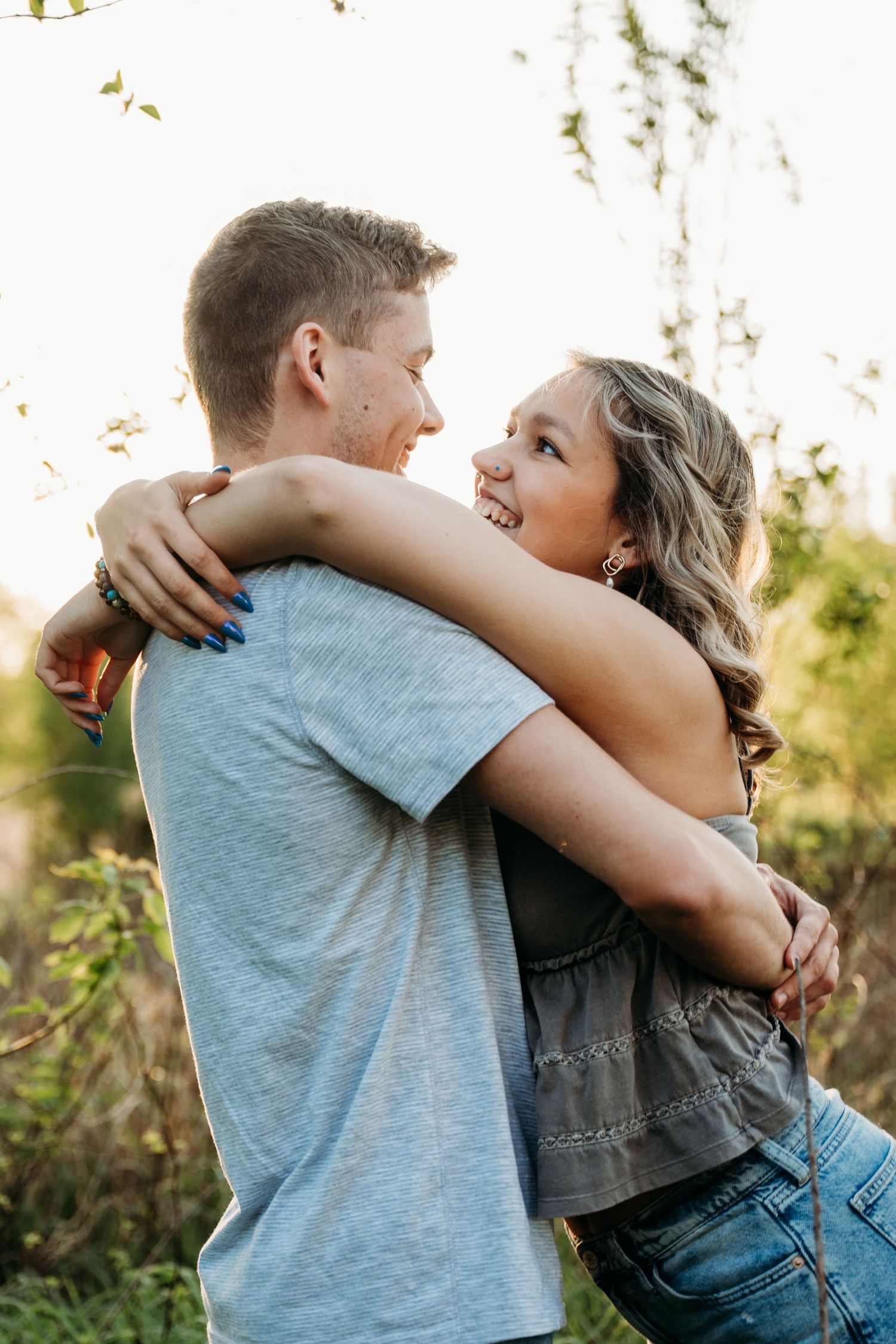 A couple shares a loving embrace outdoors during golden hour with natural foliage in the background.