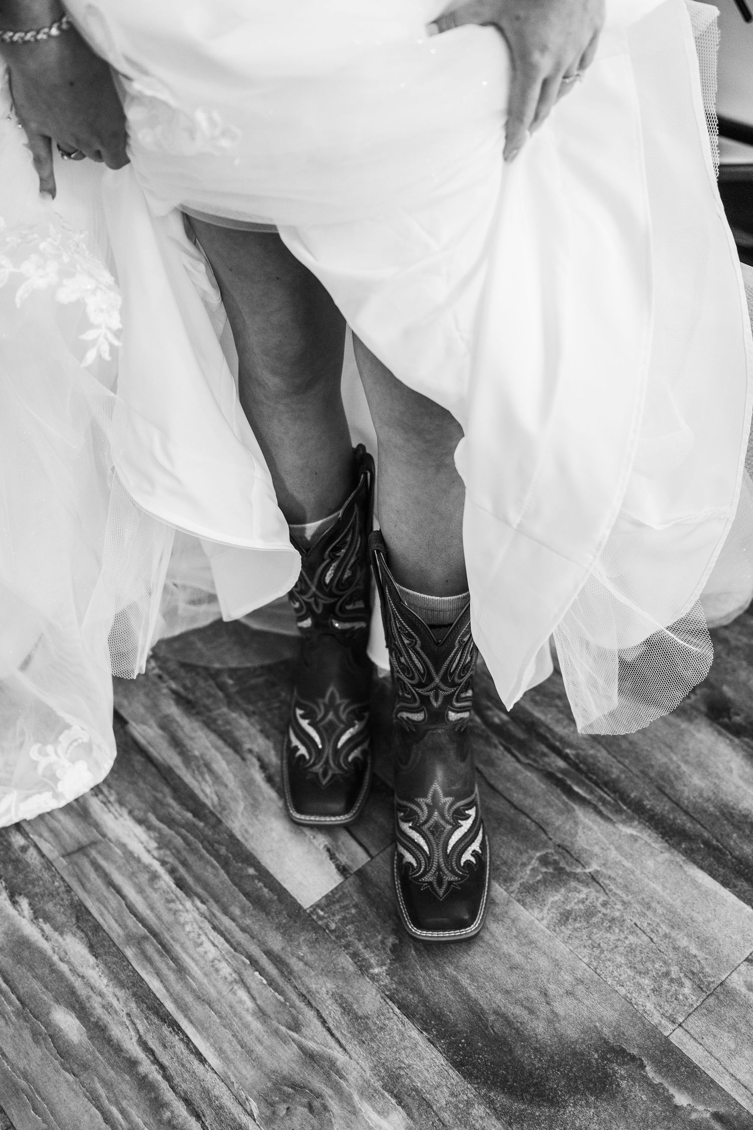 Black cowboy boots with decorative stitching peek out from under a white wedding dress.