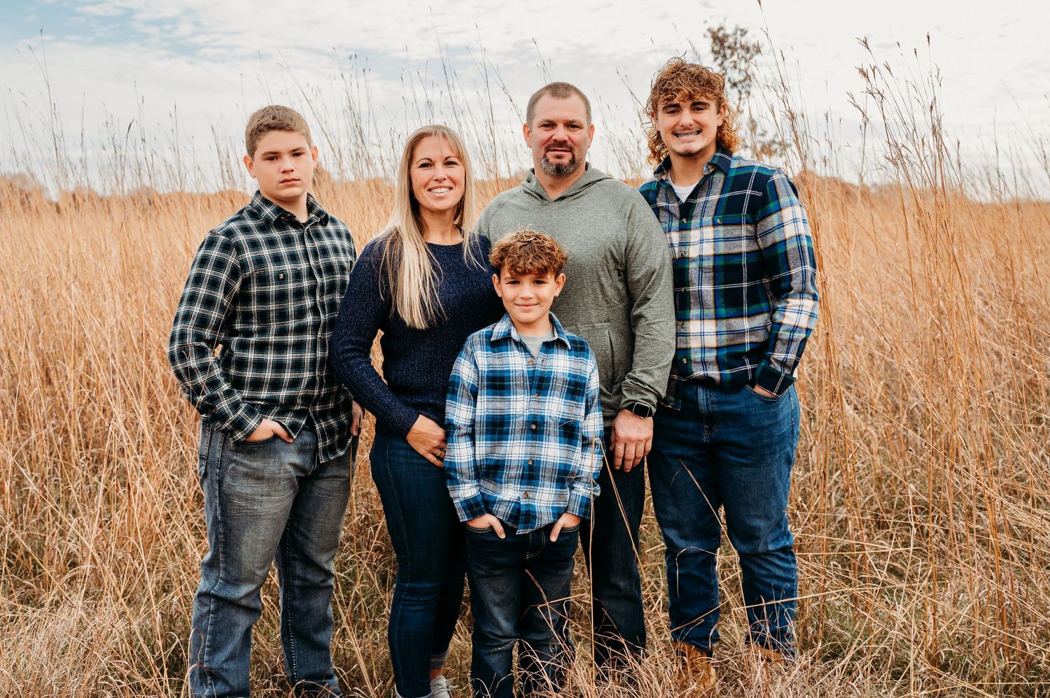 A group of people wearing plaid shirts and casual attire pose together in a field of tall autumn grass.