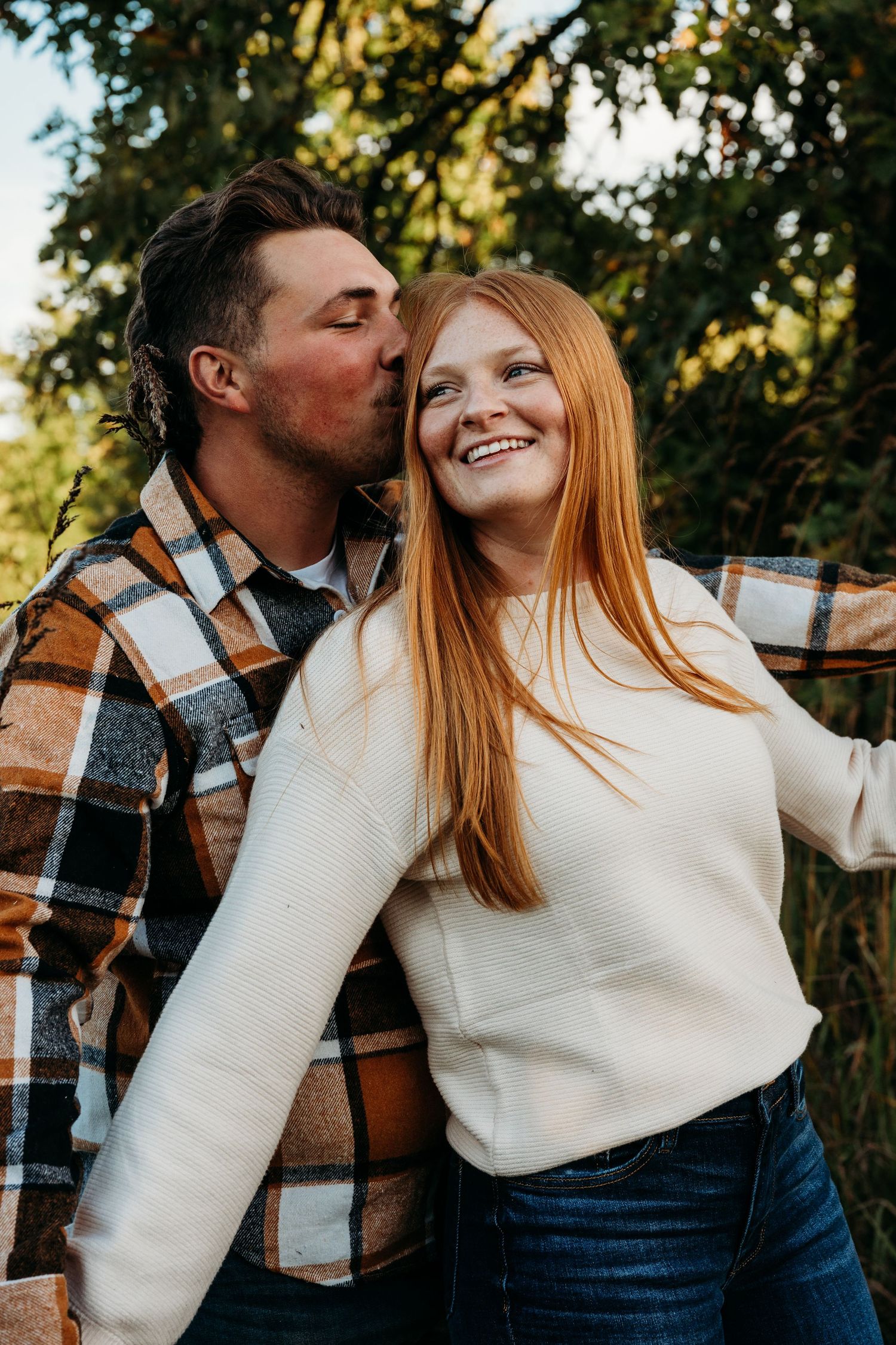 Couple sharing romantic moments in white sweater and plaid shirt against outdoor autumn setting.