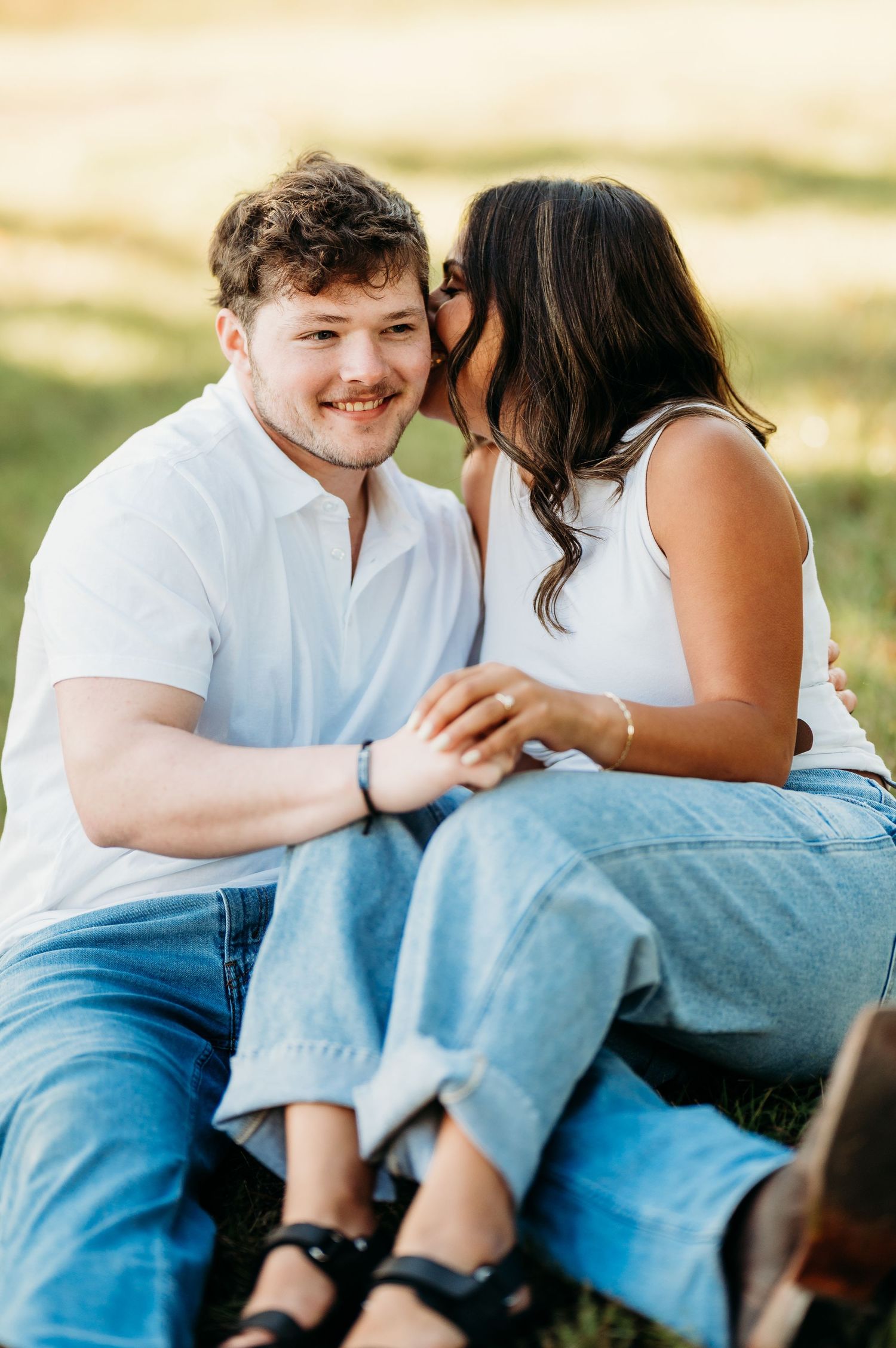 Couple in casual attire sharing intimate moments while sitting together outdoors in warm sunlight.