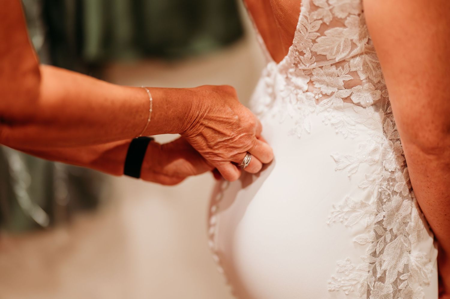 Close-up of hands fastening delicate buttons on a white lace wedding dress.