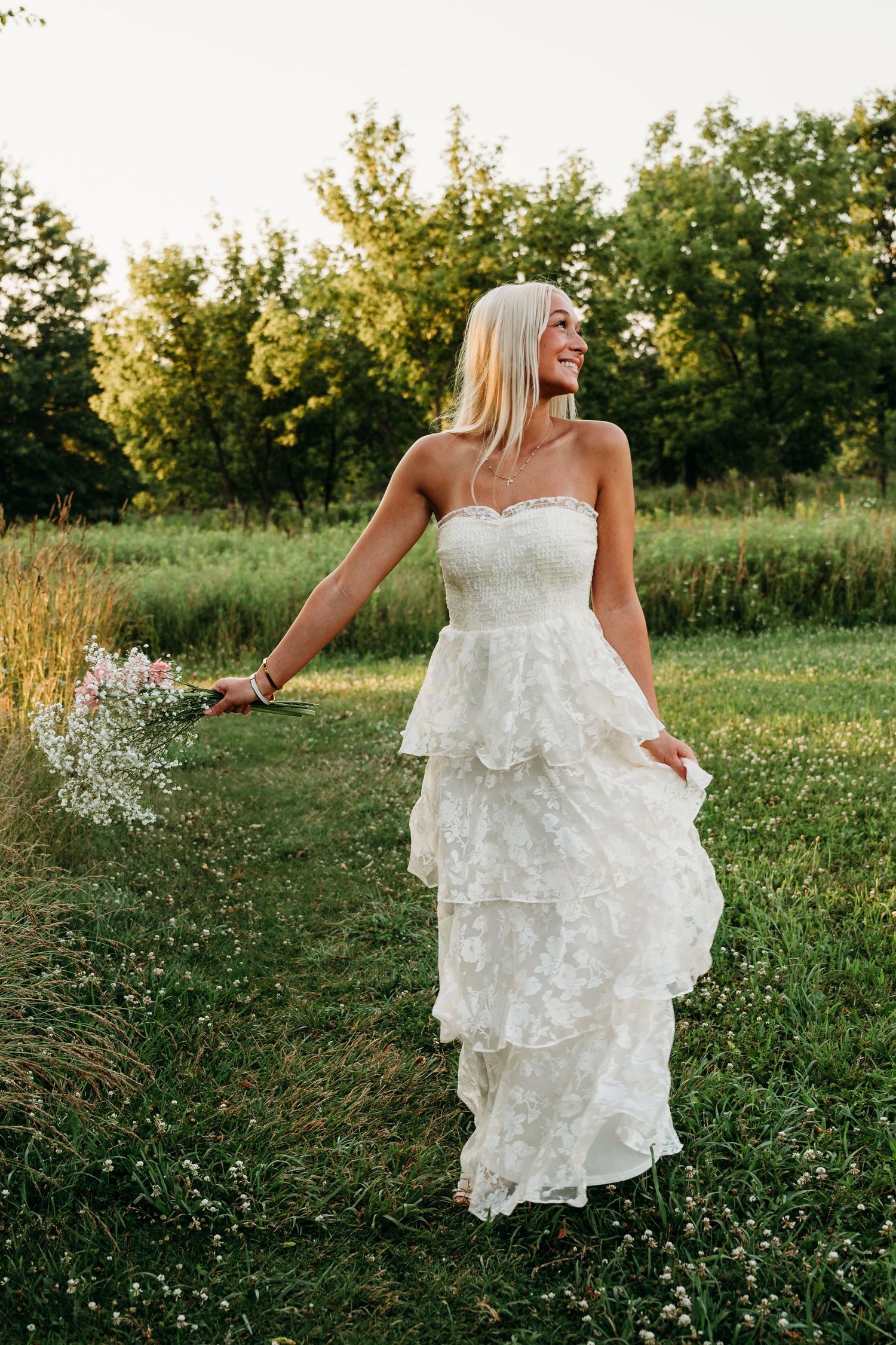 A white lace wedding dress flows elegantly as someone walks through a sunlit meadow at golden hour.