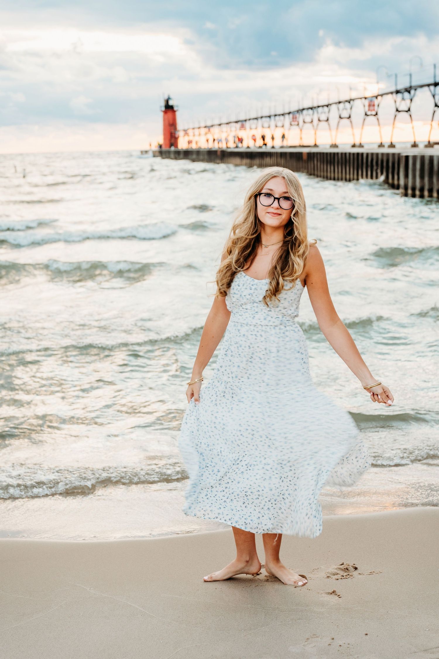 Playful beachside photos show someone in a white dress dancing near a lighthouse and pier at sunset.