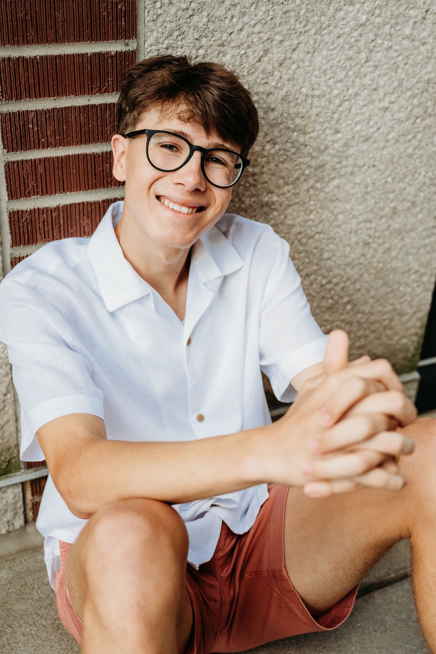 Young person in glasses and white shirt sits casually against wall in multi-frame collage series.