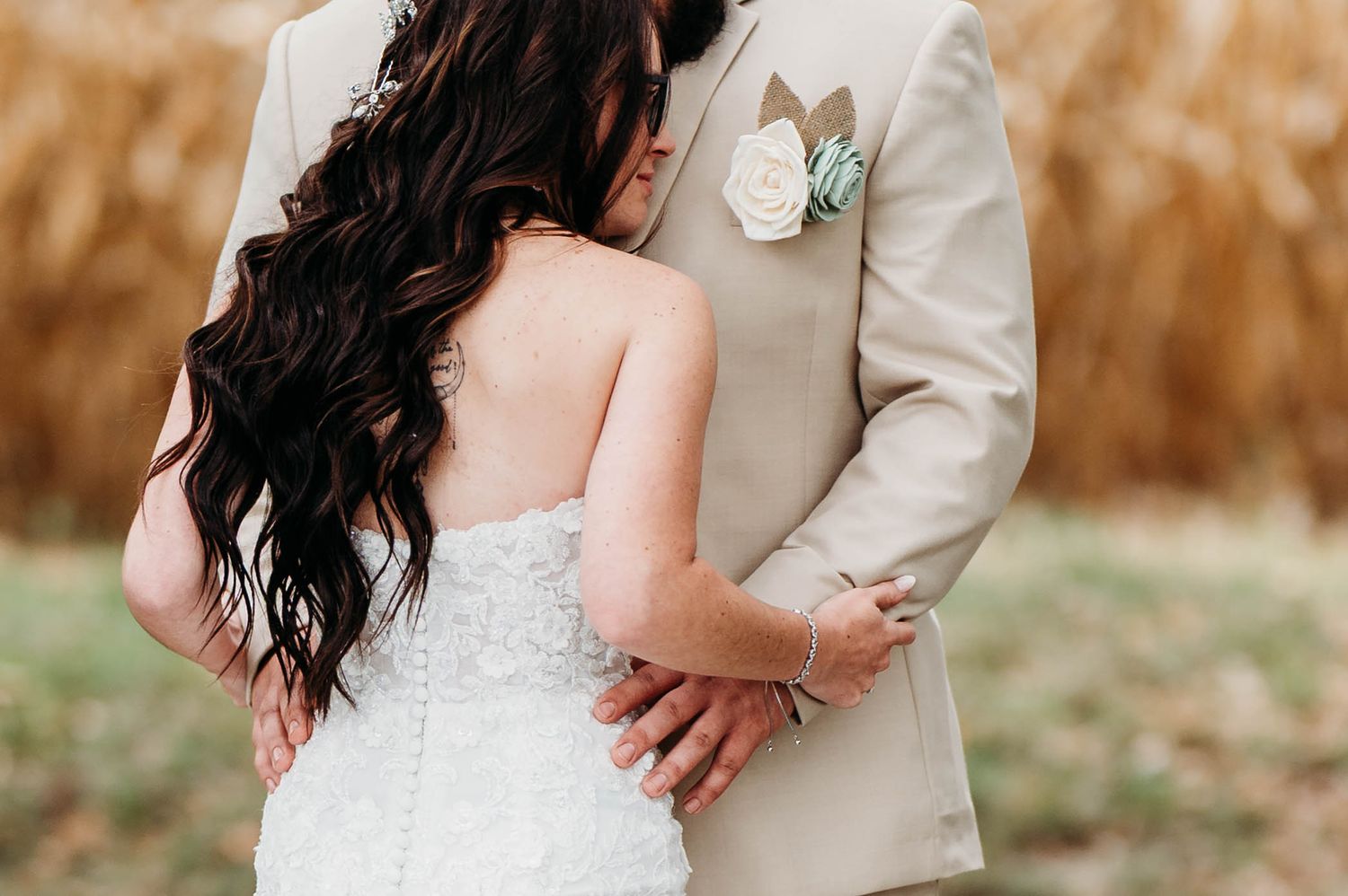 Romantic wedding couple embraces in a rustic outdoor setting with autumn colors in the background.