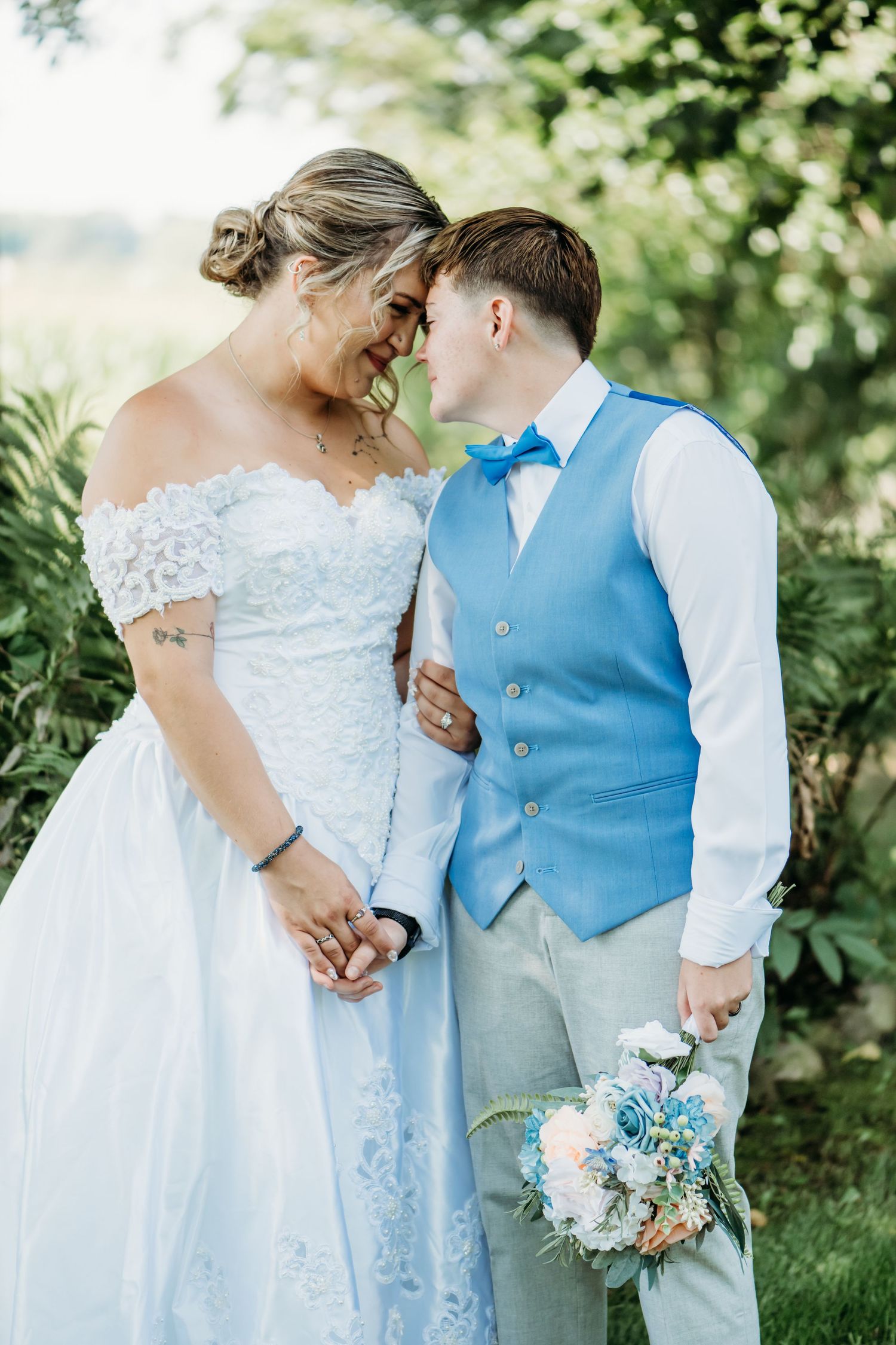 A romantic wedding moment captured outdoors with a couple in blue and white attire sharing an intimate moment among greenery.