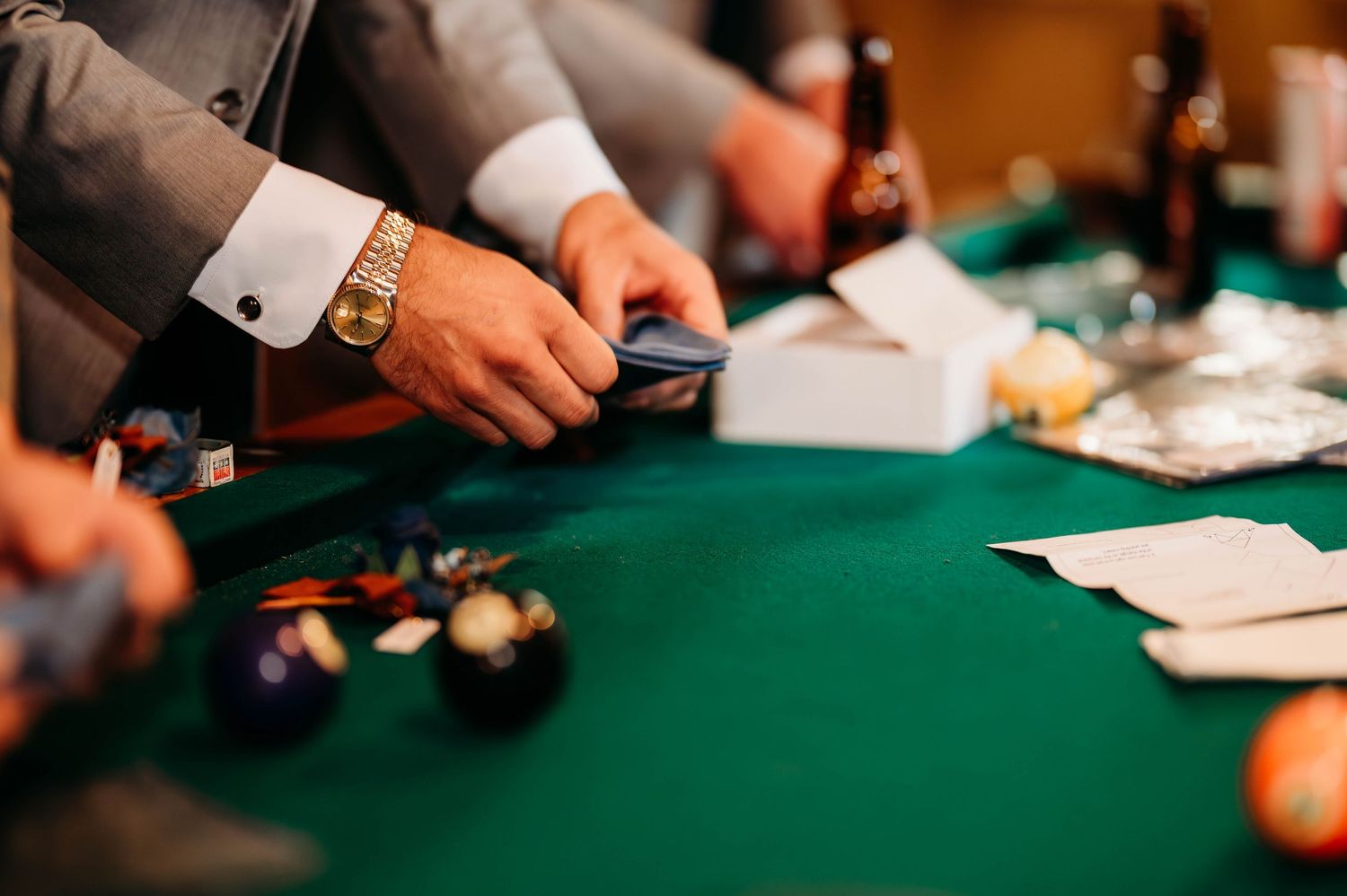 Hands of poker players around a green felt table with playing cards and chips visible during gameplay.