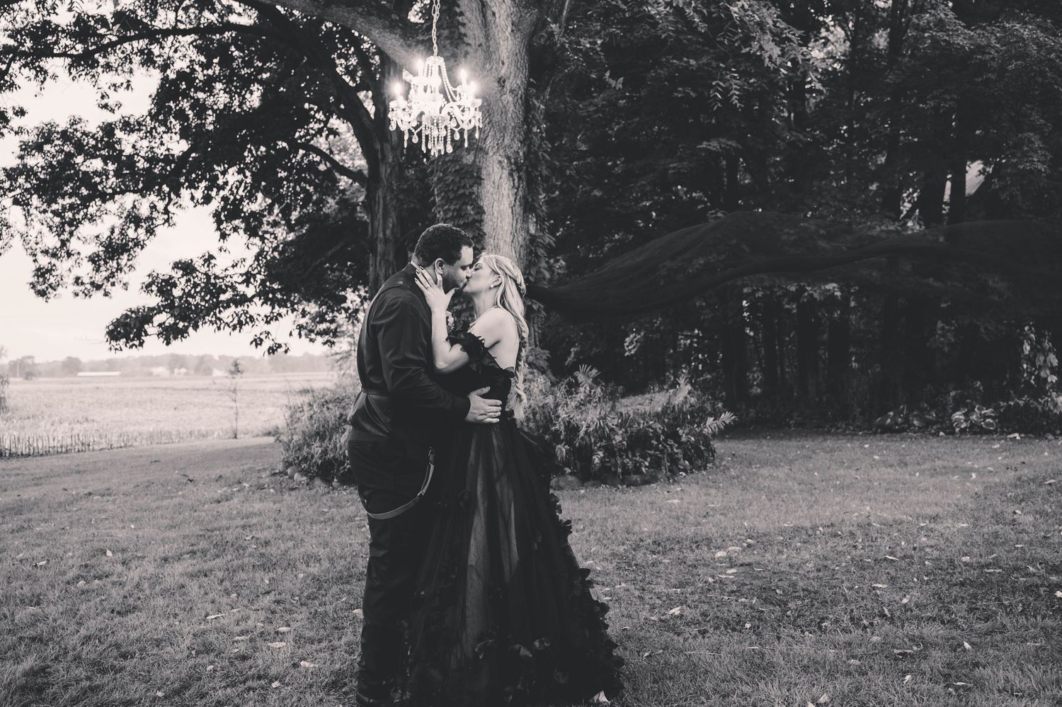 Black and white photo series showing a couple embracing outdoors under trees during a romantic engagement session.