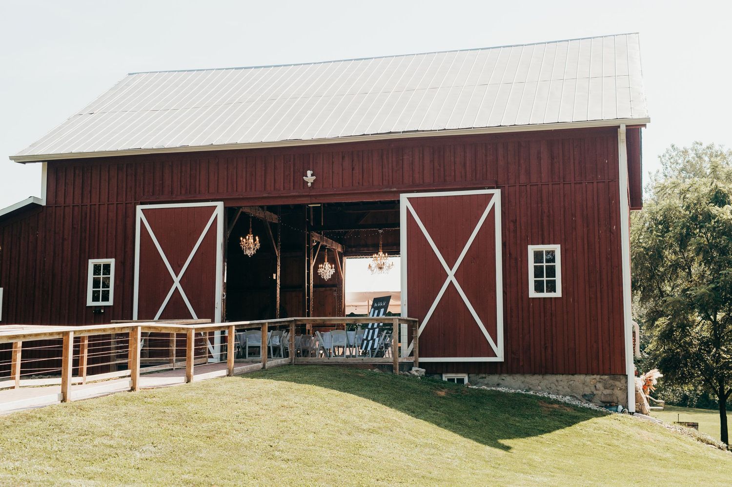 A panoramic view of multiple rustic red barns with white trim set against green farmland and trees.