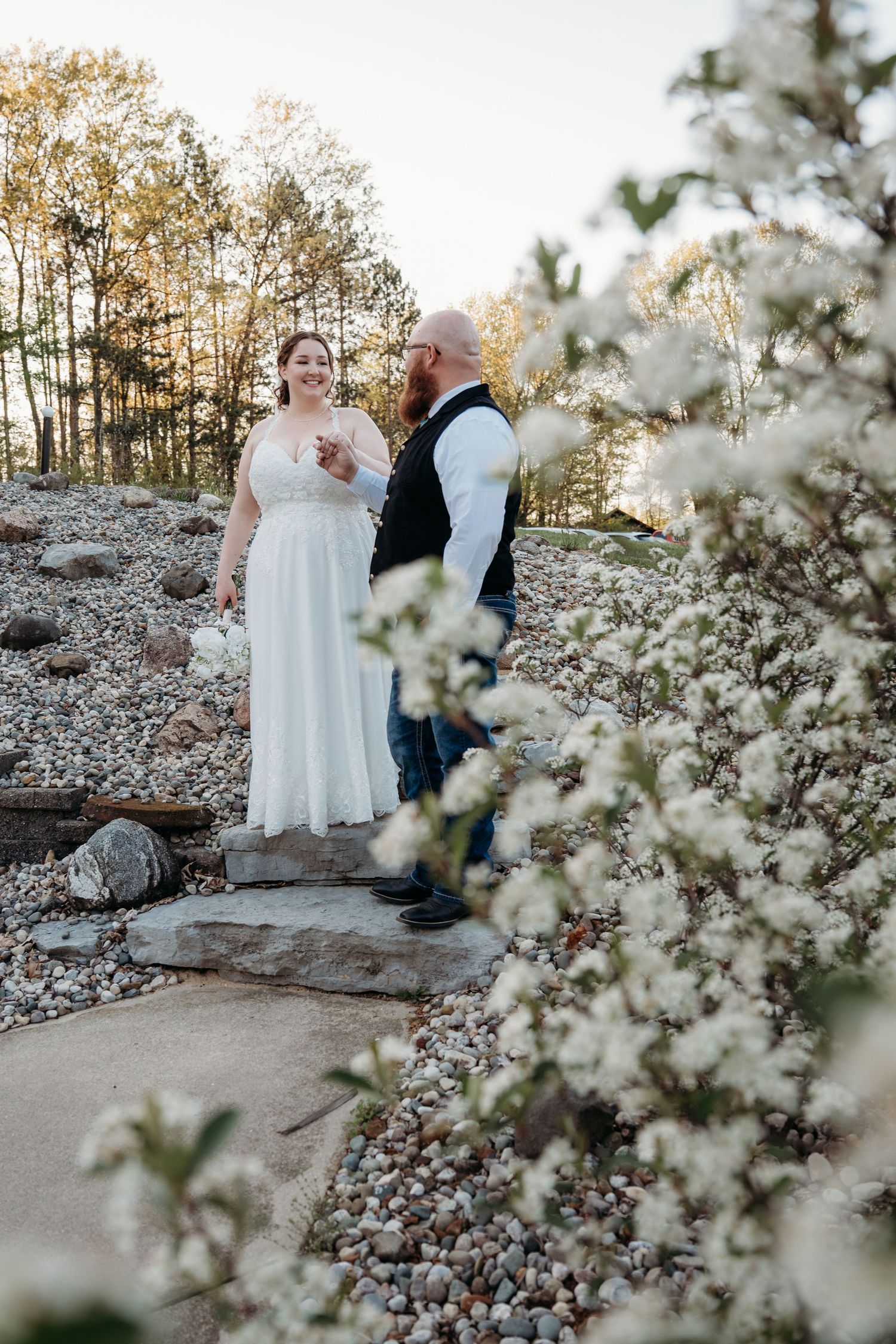 A couple shares a romantic moment among blooming white flowers on a stone pathway.