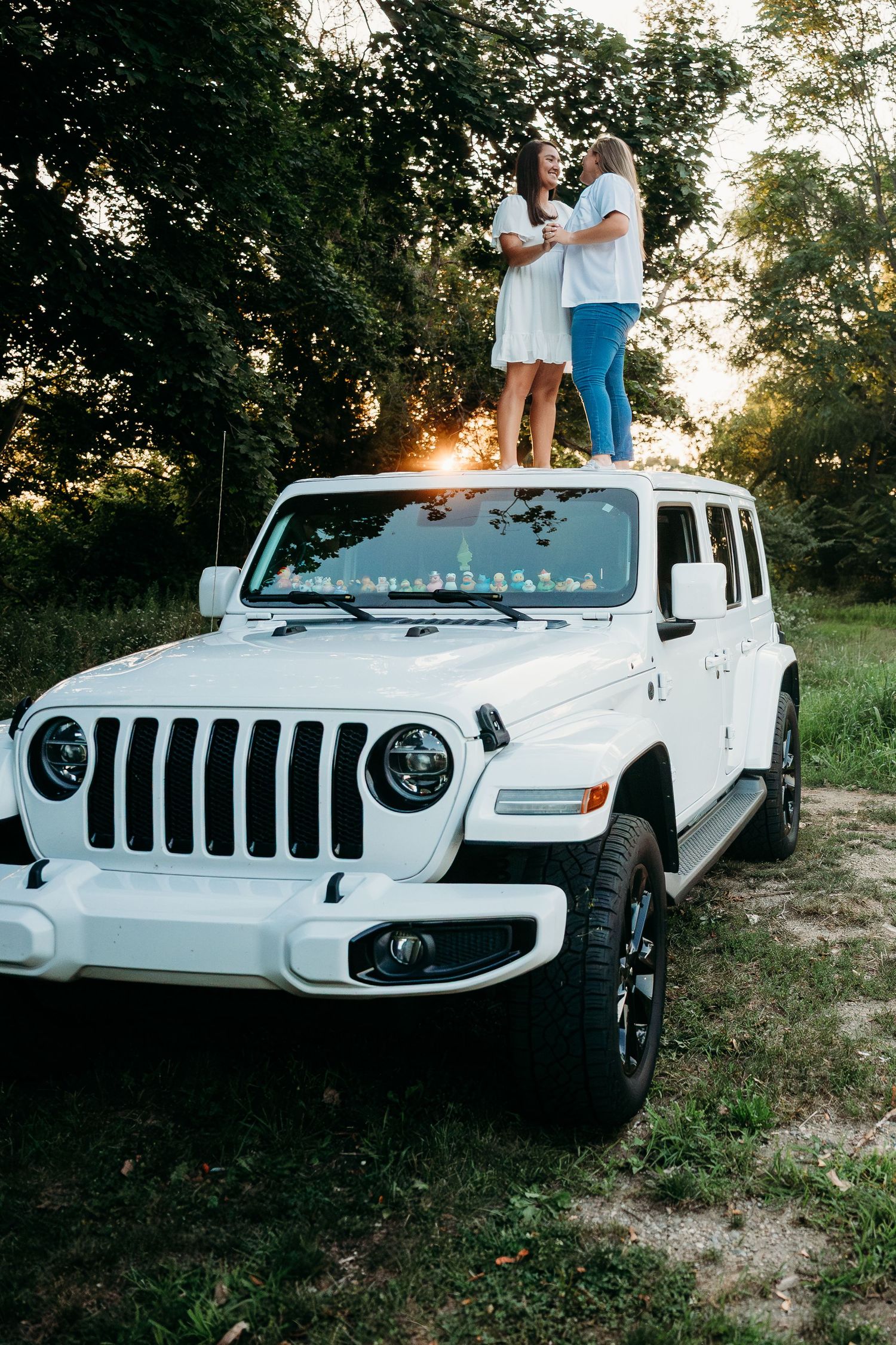 White Jeep Wrangler parked on rugged terrain during golden hour sunset with trees in background.