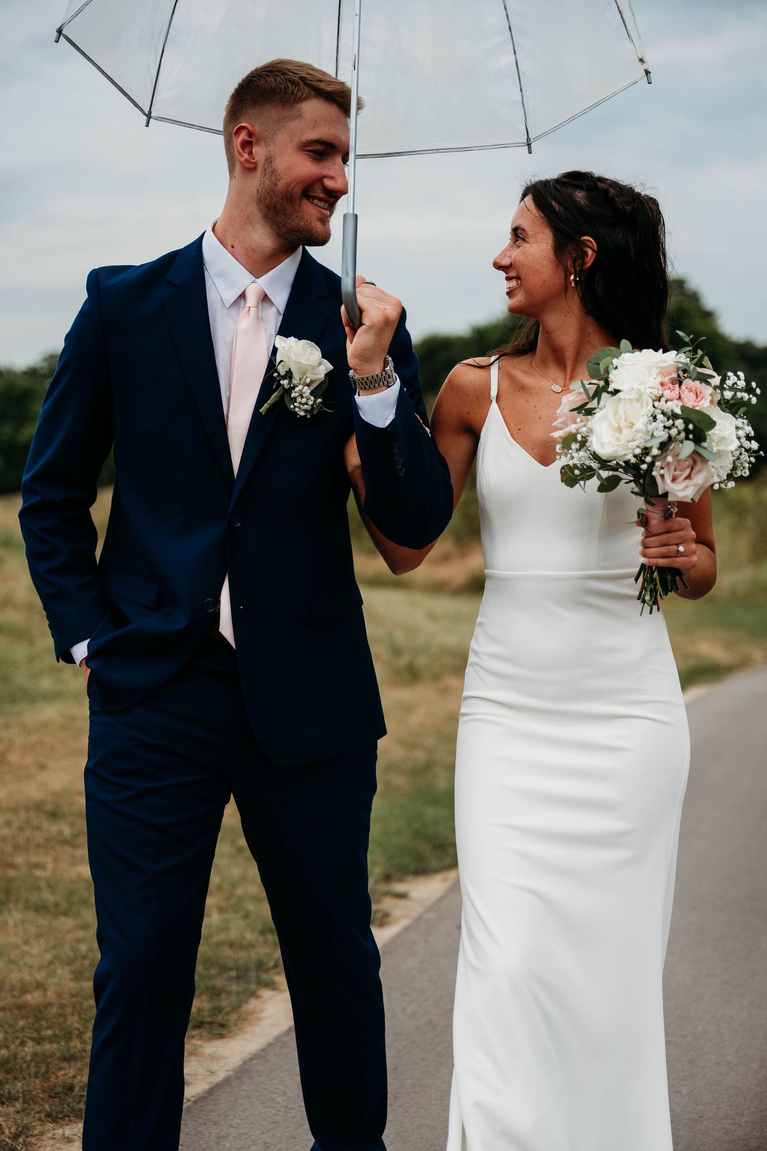 A couple shares a playful moment under a white umbrella, with the bride in white and groom in navy blue.