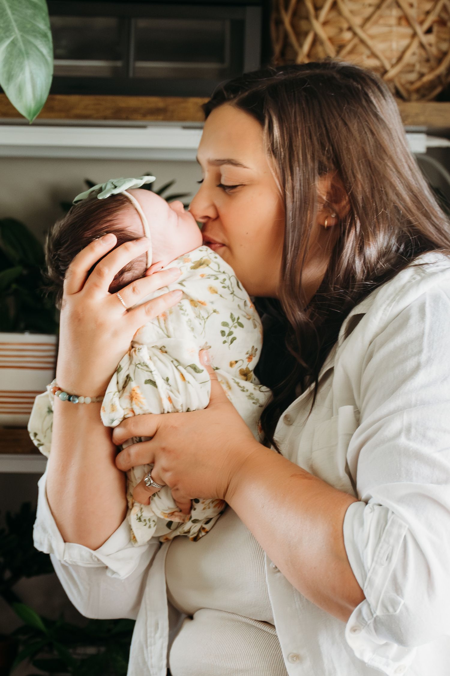 A tender moment captured as a parent in a white shirt gives a gentle kiss to their baby wearing a floral print outfit.