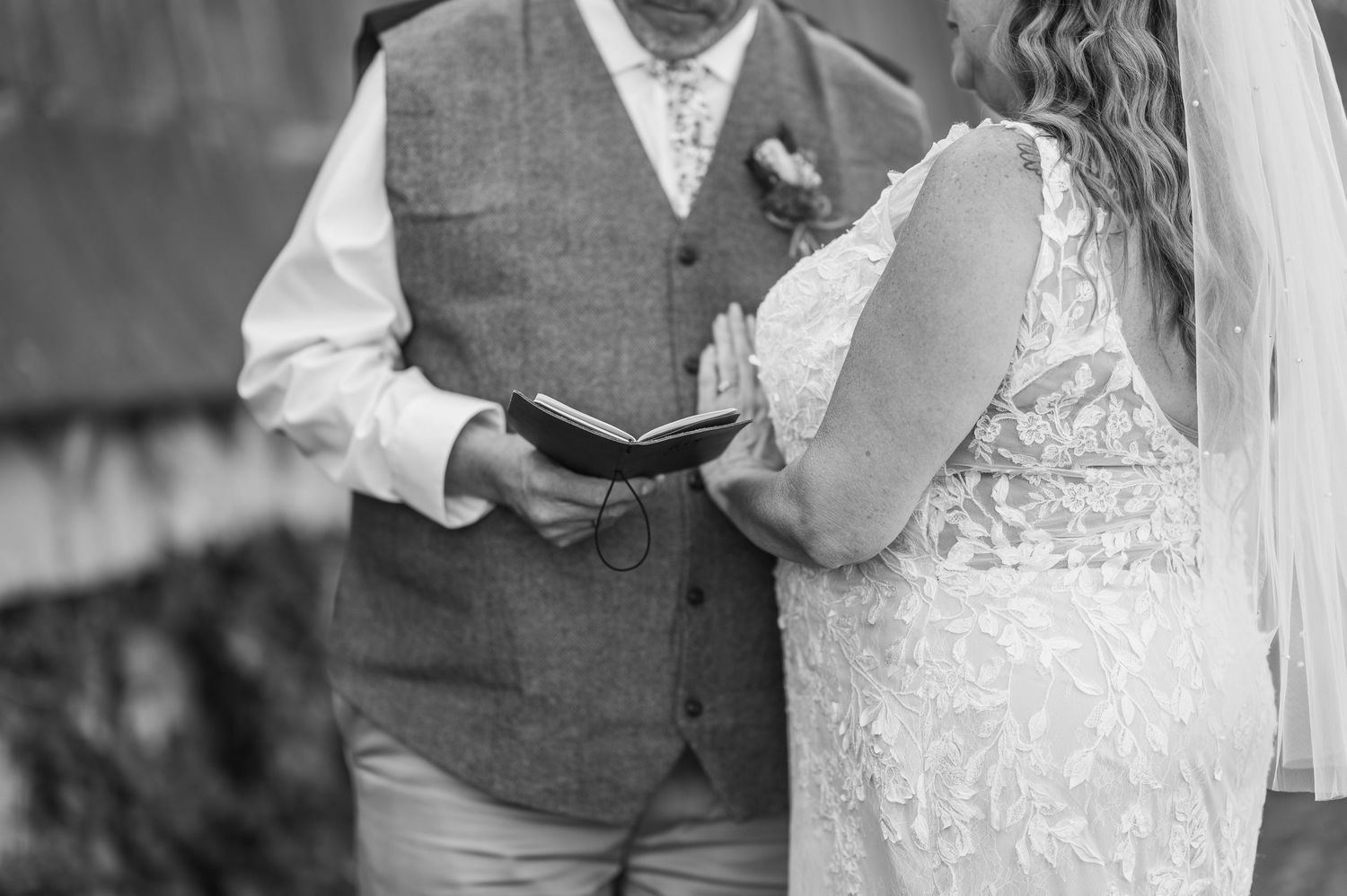 A black and white photo of a couple exchanging vows during an outdoor wedding ceremony.