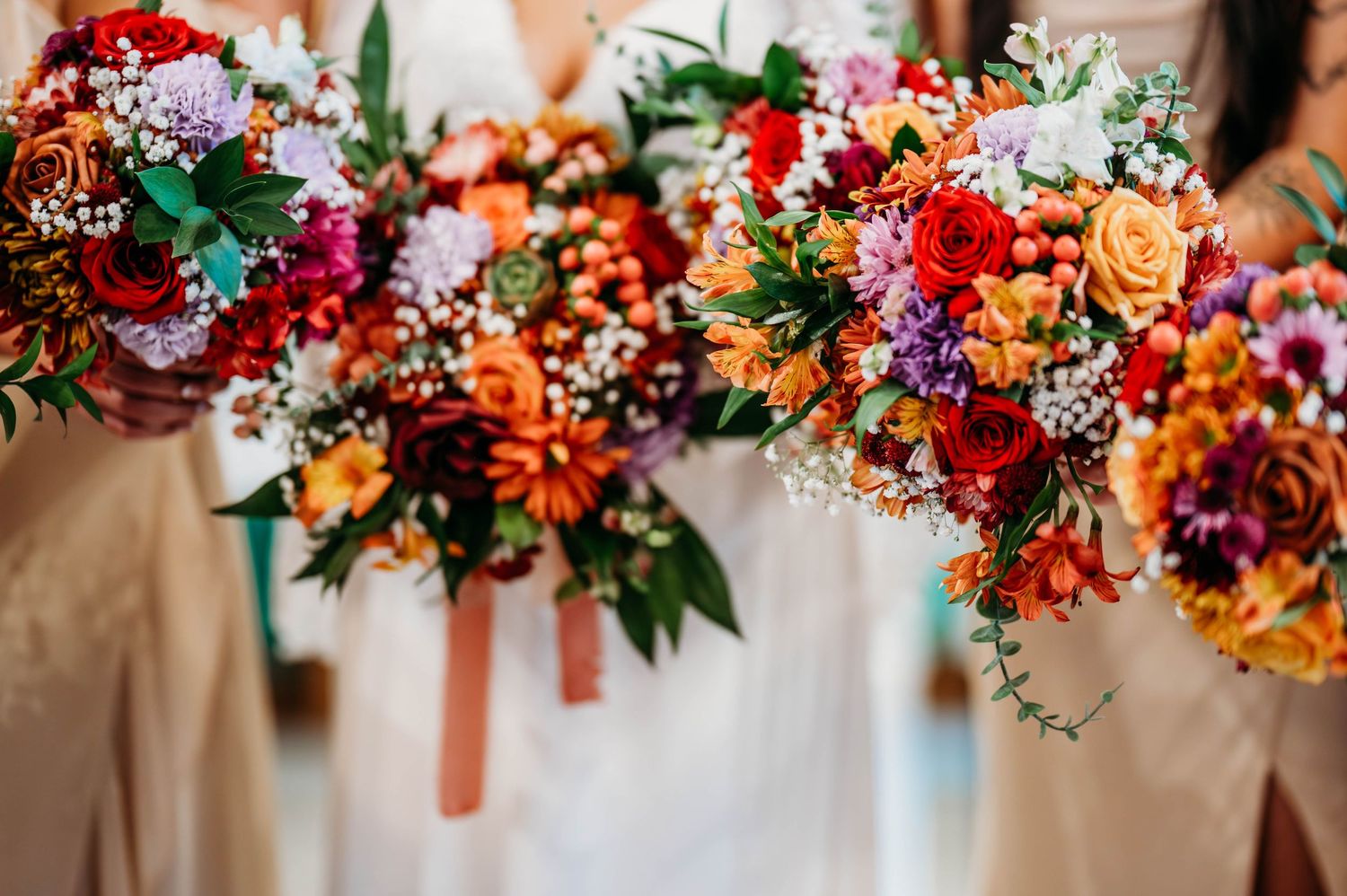 Colorful floral wedding arch decorations with vibrant orange and pink blooms hanging from a rustic wooden frame.