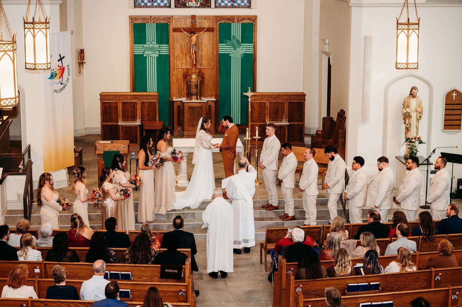 Traditional church wedding ceremony with guests seated in wooden pews and clergy in white robes at the altar.