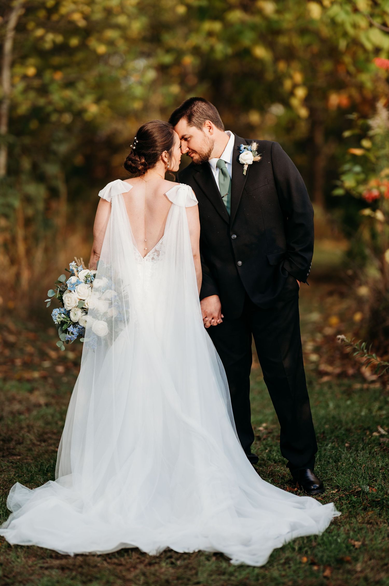 Romantic outdoor wedding couple in black suit and flowing white dress pose together in autumn woodland setting.