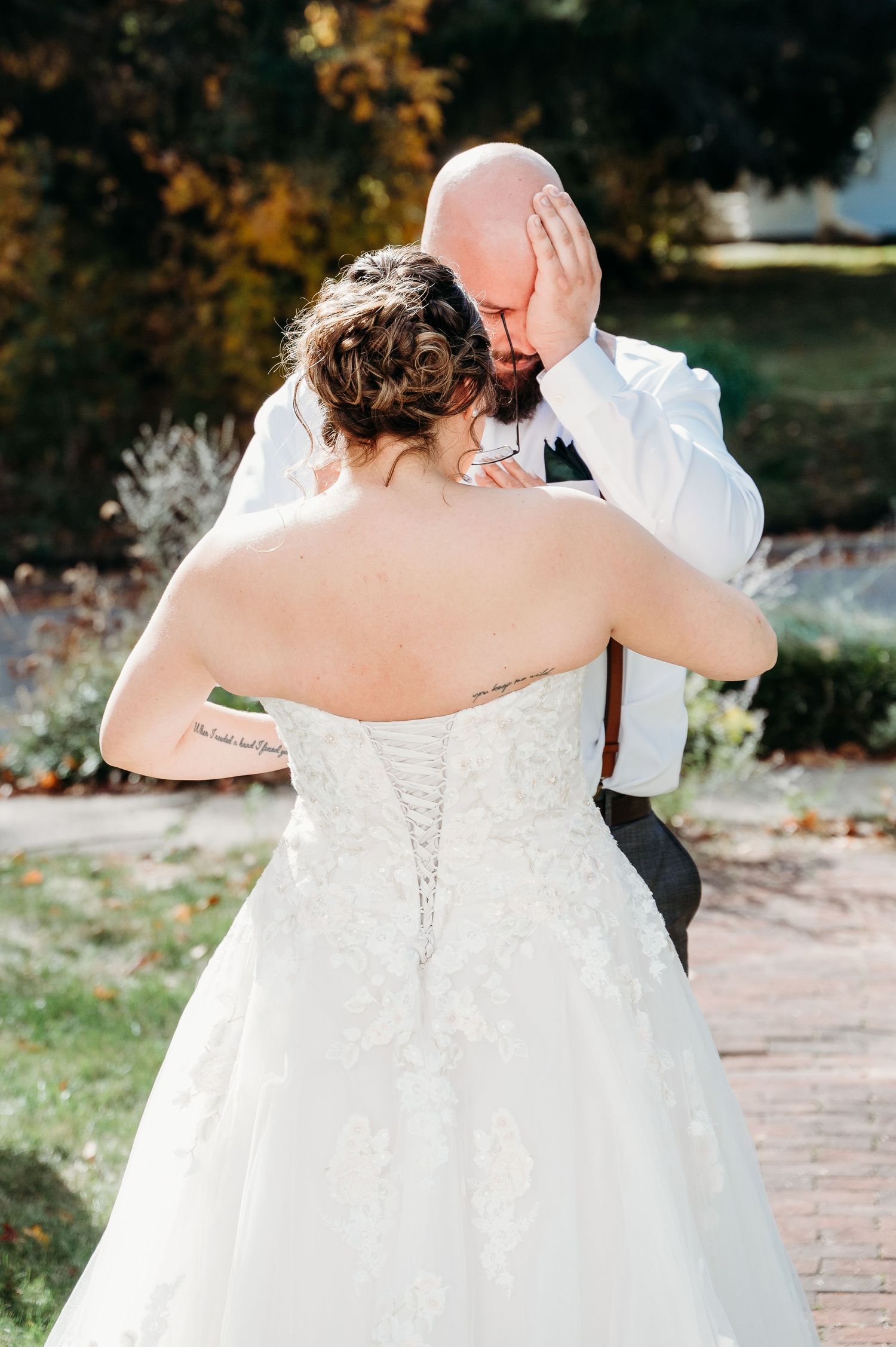 Couple shares intimate moment in outdoor garden setting wearing wedding attire with lace corset dress and white shirt.