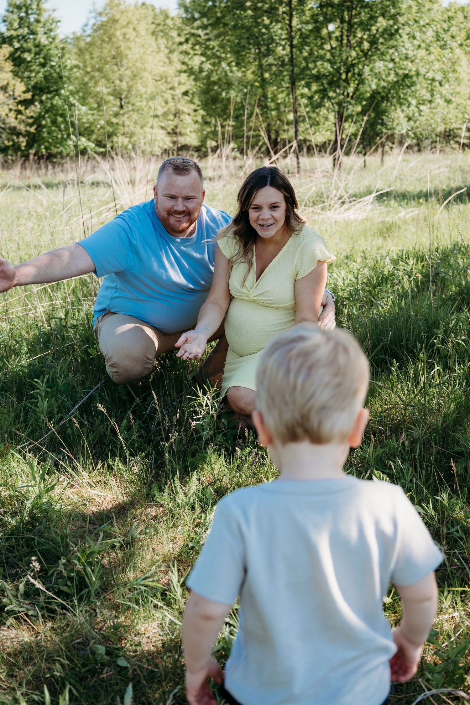 A family enjoys a playful outdoor moment together on green grass with trees in the background.