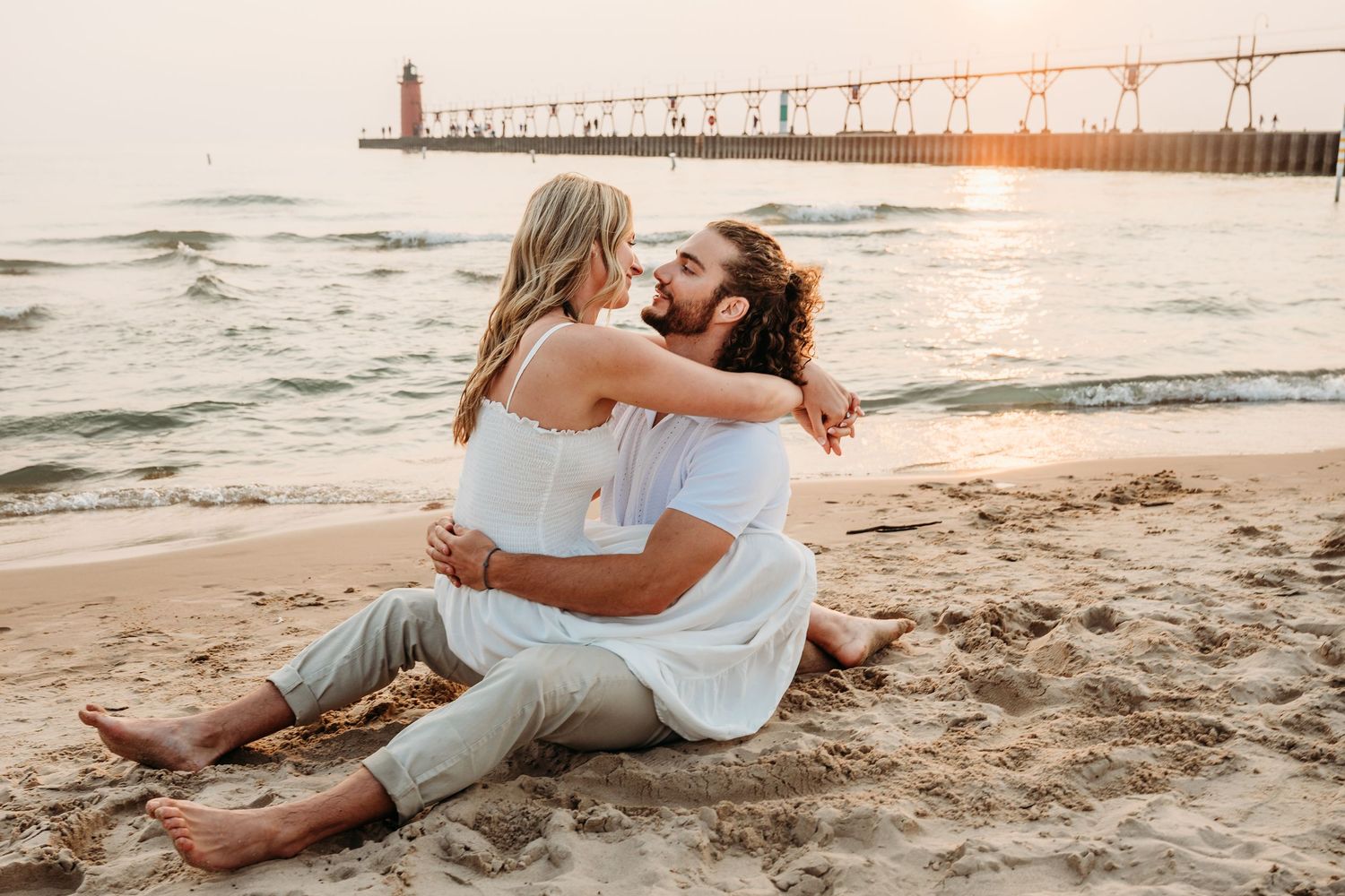 A warm-toned coastal engagement session captures candid moments between a couple on sandy shores.