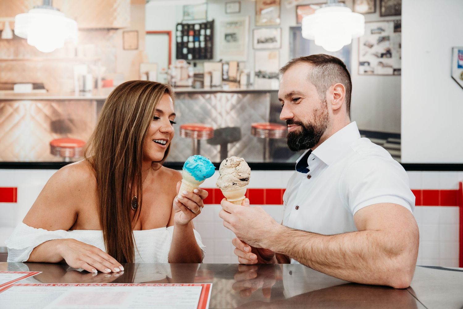 A couple laughs together while sitting at a white retro diner counter.