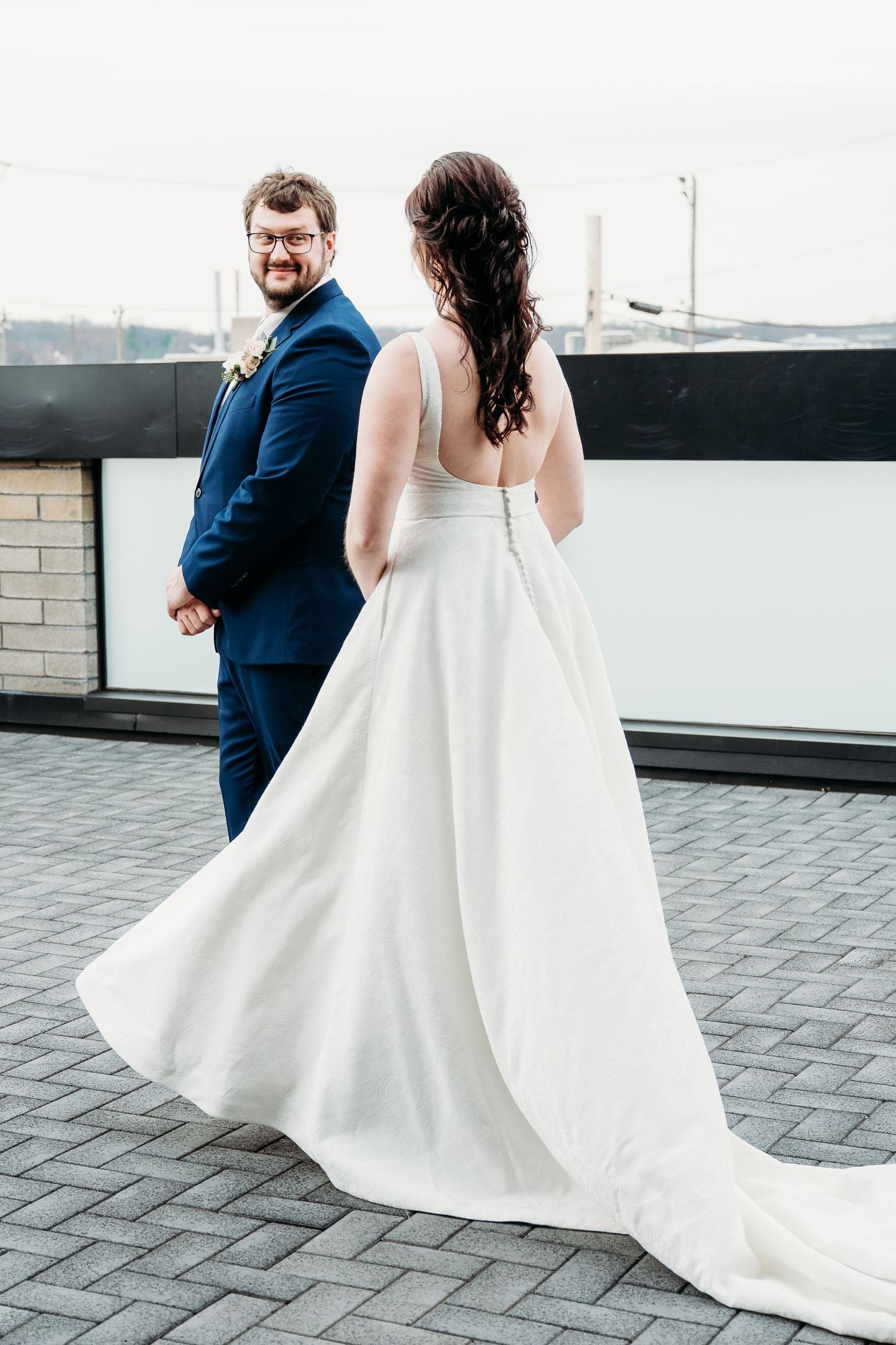 A couple on their wedding day shows the elegant flowing white dress and navy blue suit on a rooftop setting.