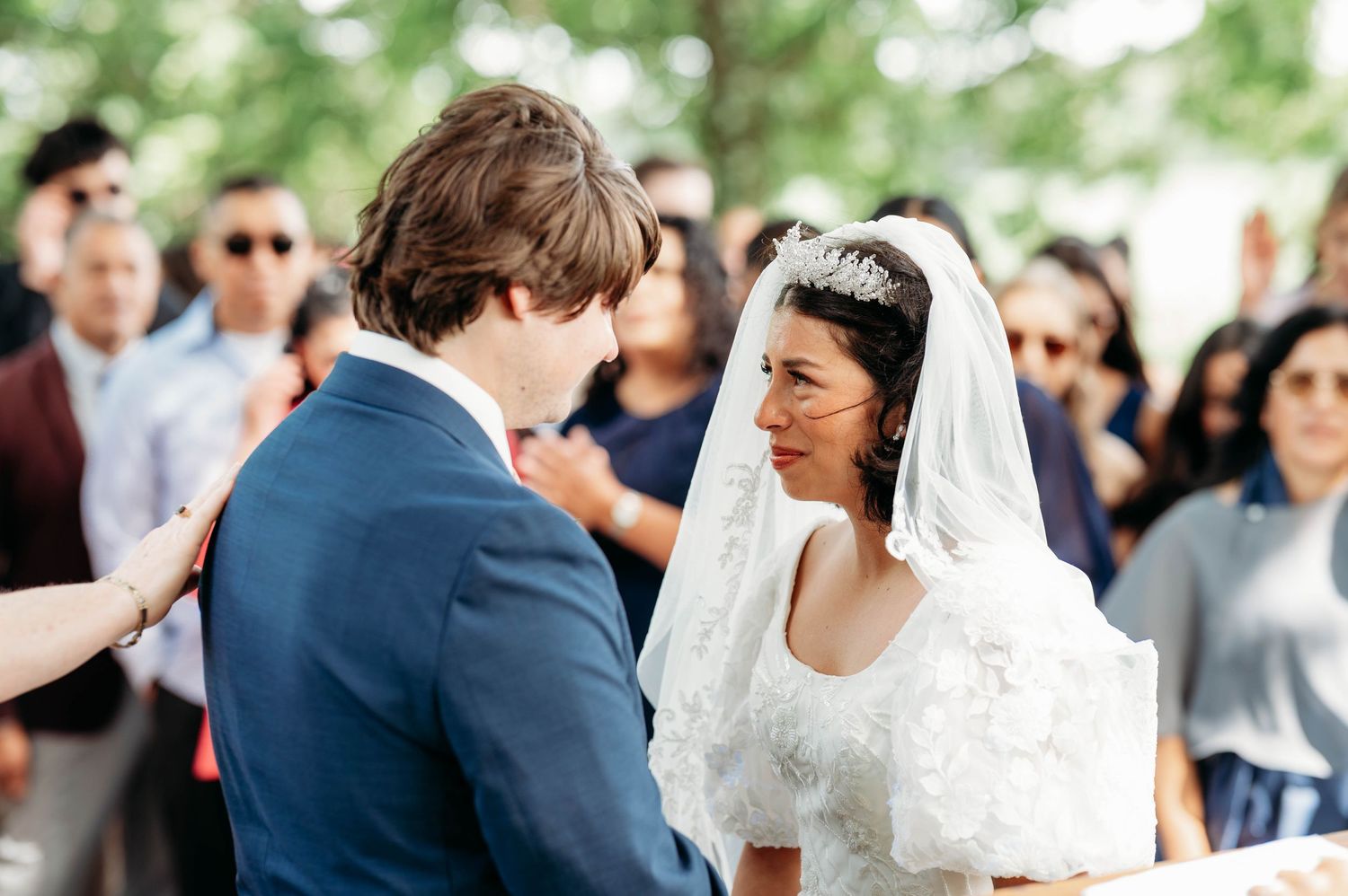 Bride and groom share an intimate moment during outdoor wedding ceremony, bride wearing lace veil and tiara.