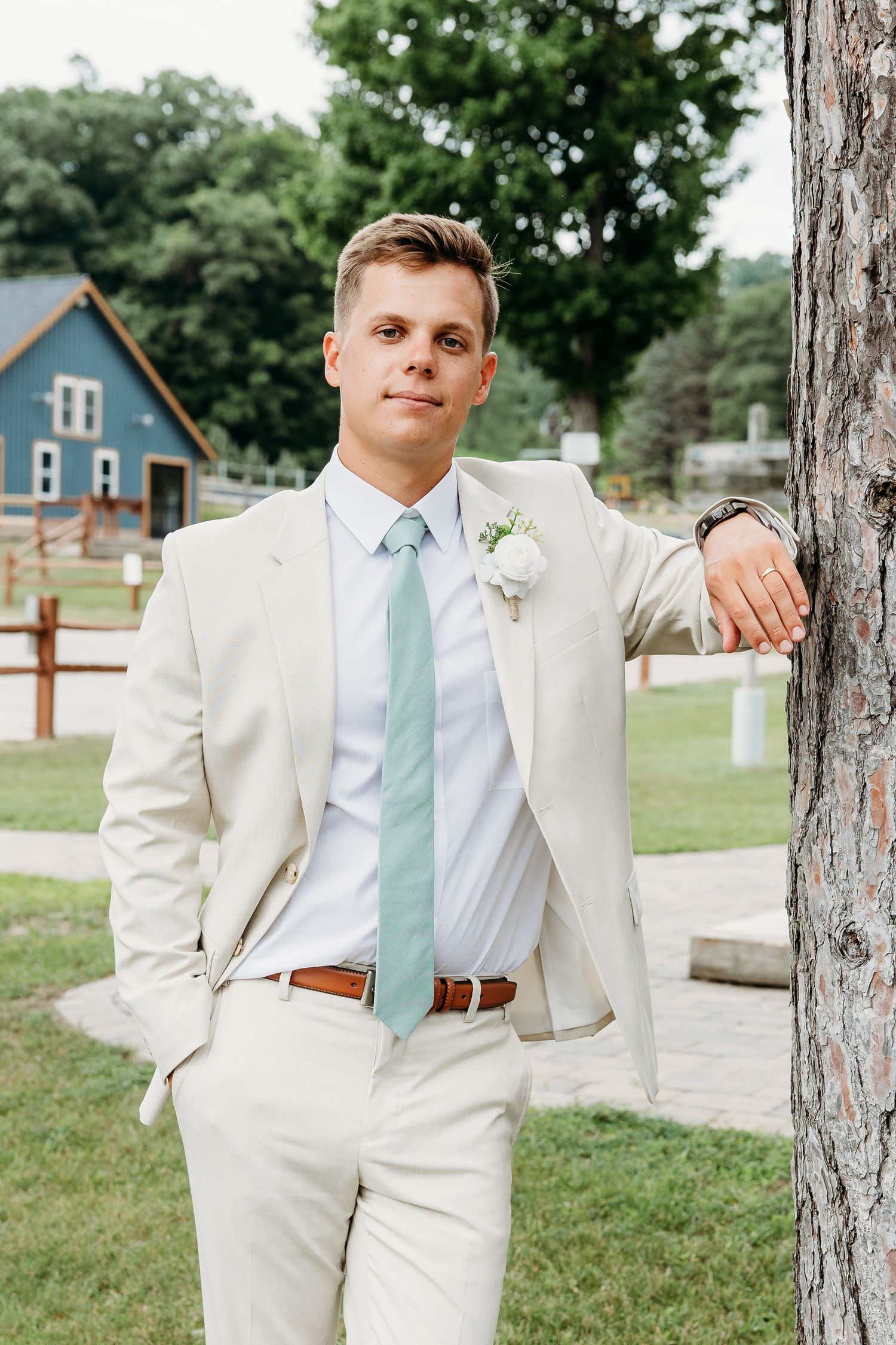 Groomsmen in light beige suits with mint green ties pose casually against rustic wooden posts outdoors.
