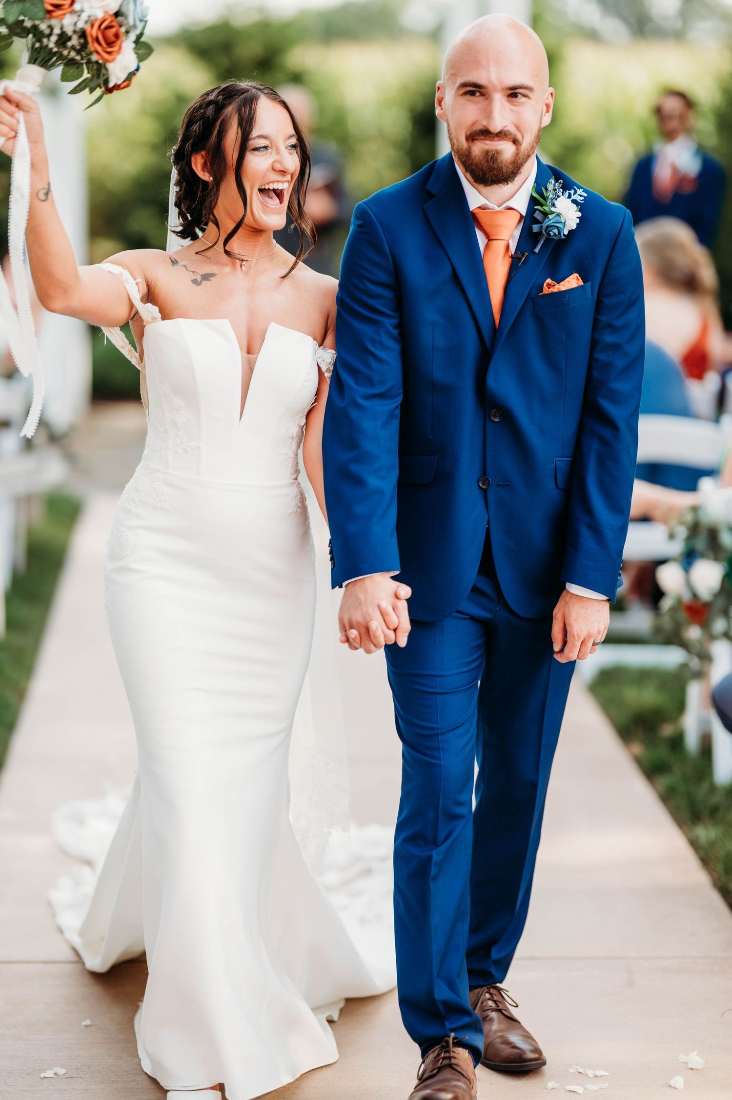 A couple in wedding attire, with a bride in white dress and groom in navy blue suit, walking together outdoors.