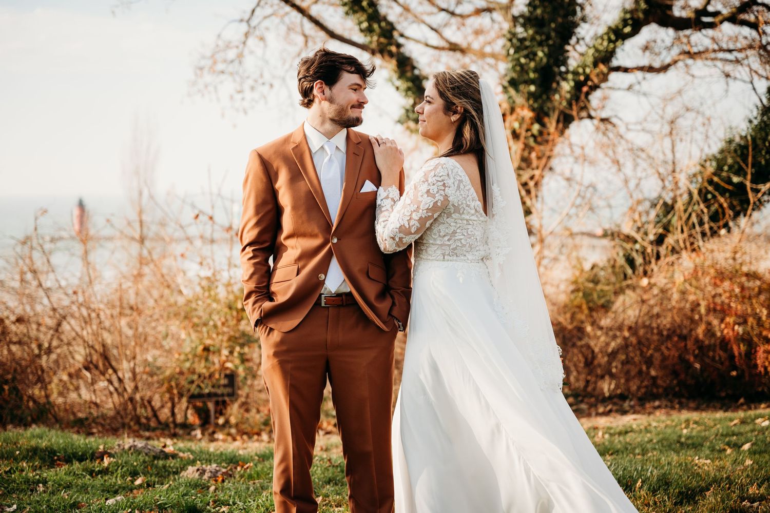 A bride in a white gown and groom in a brown suit share a romantic moment outdoors on their wedding day. West Mi Wedding Photographer