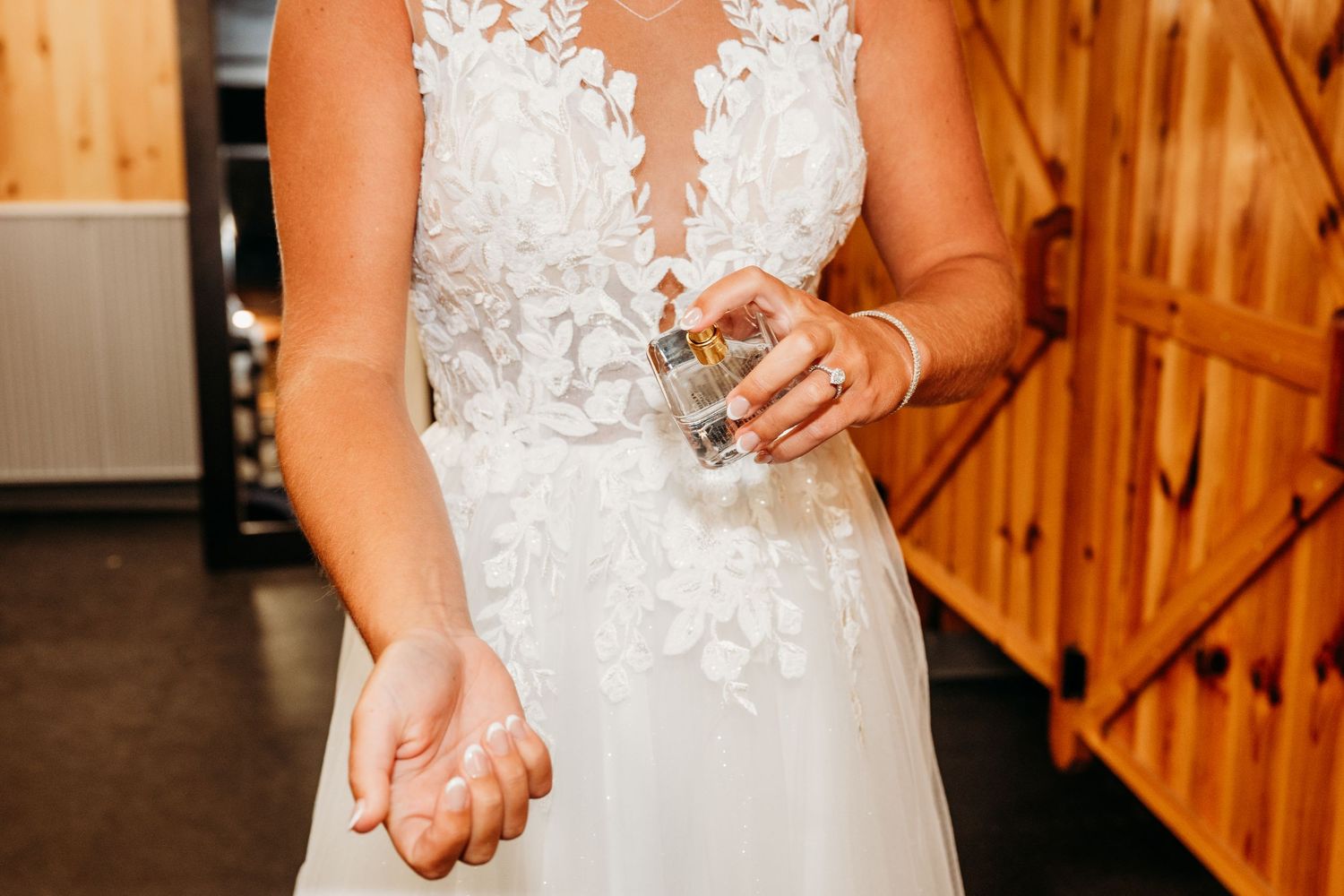 Bride in lace wedding gown spraying perfume on her wrist before the ceremony.