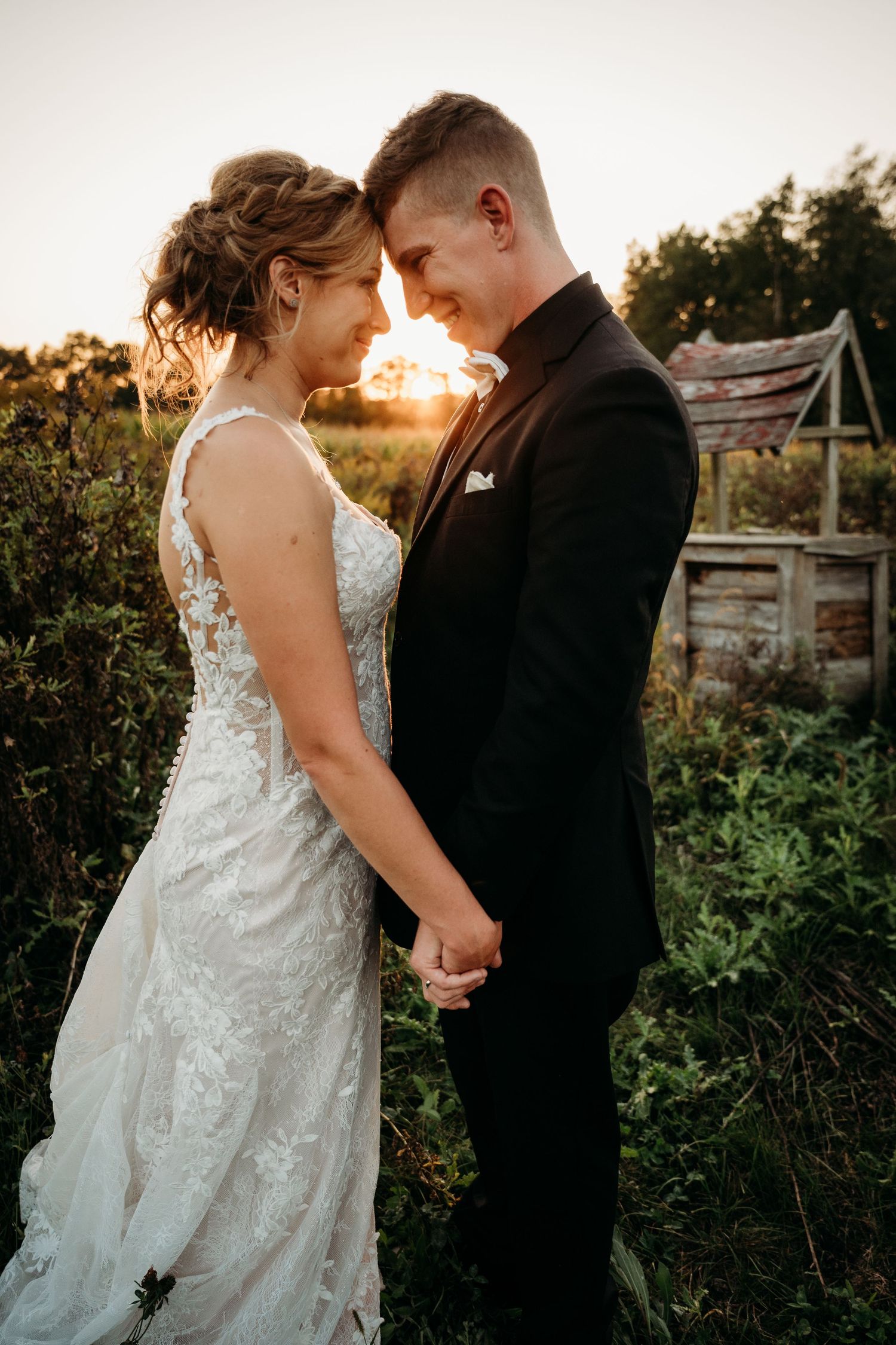 A couple shares intimate moments in a garden setting at sunset as golden light illuminates their wedding attire.