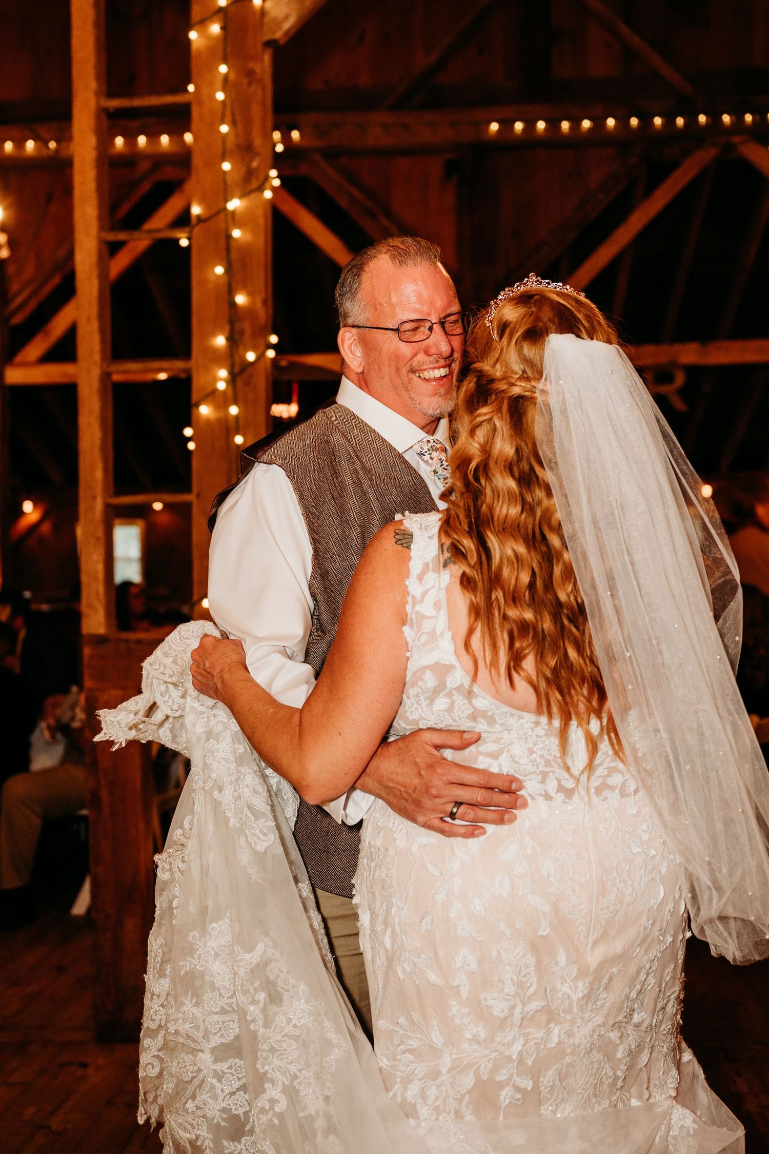 A couple shares an intimate dance moment during their wedding reception in a rustic barn with twinkling lights.