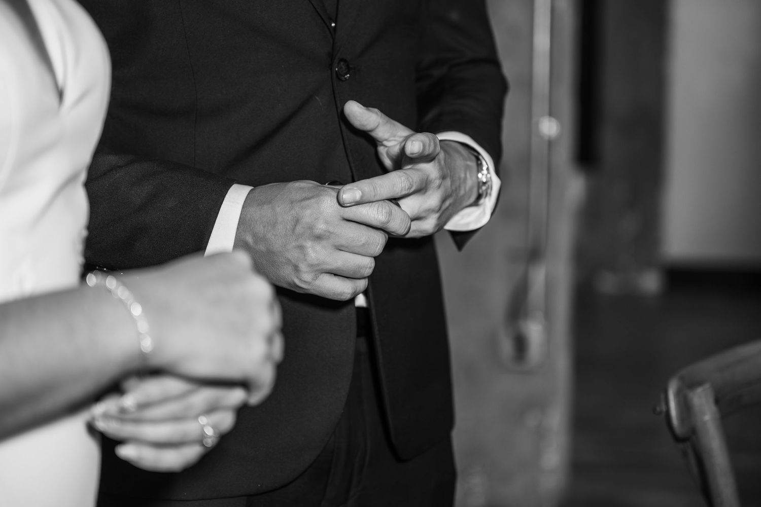Close-up black and white shot of hands adjusting formal attire during a wedding preparation.