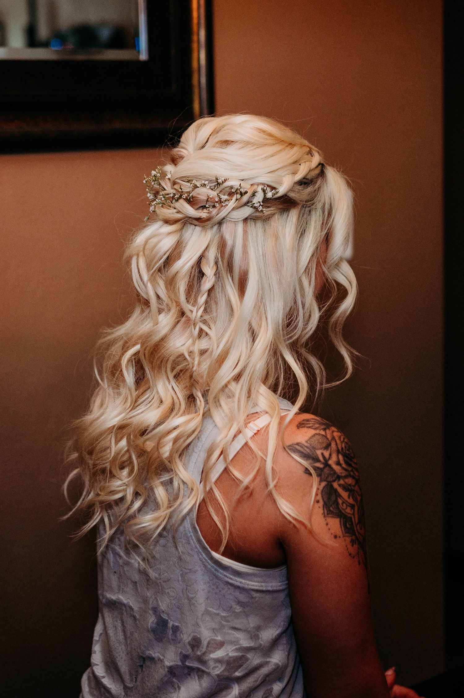 A braided crown adorns long wavy platinum blonde hair styled in romantic loose curls for a wedding or special occasion.