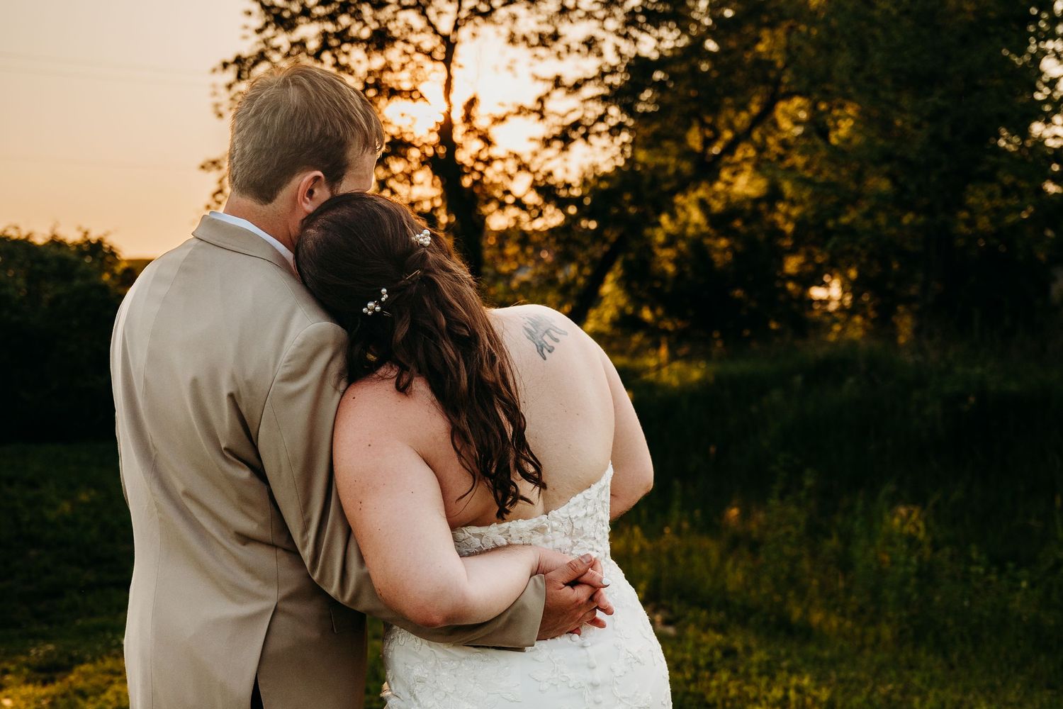 A couple embraces while watching the sunset in a scenic outdoor setting during their wedding celebration.