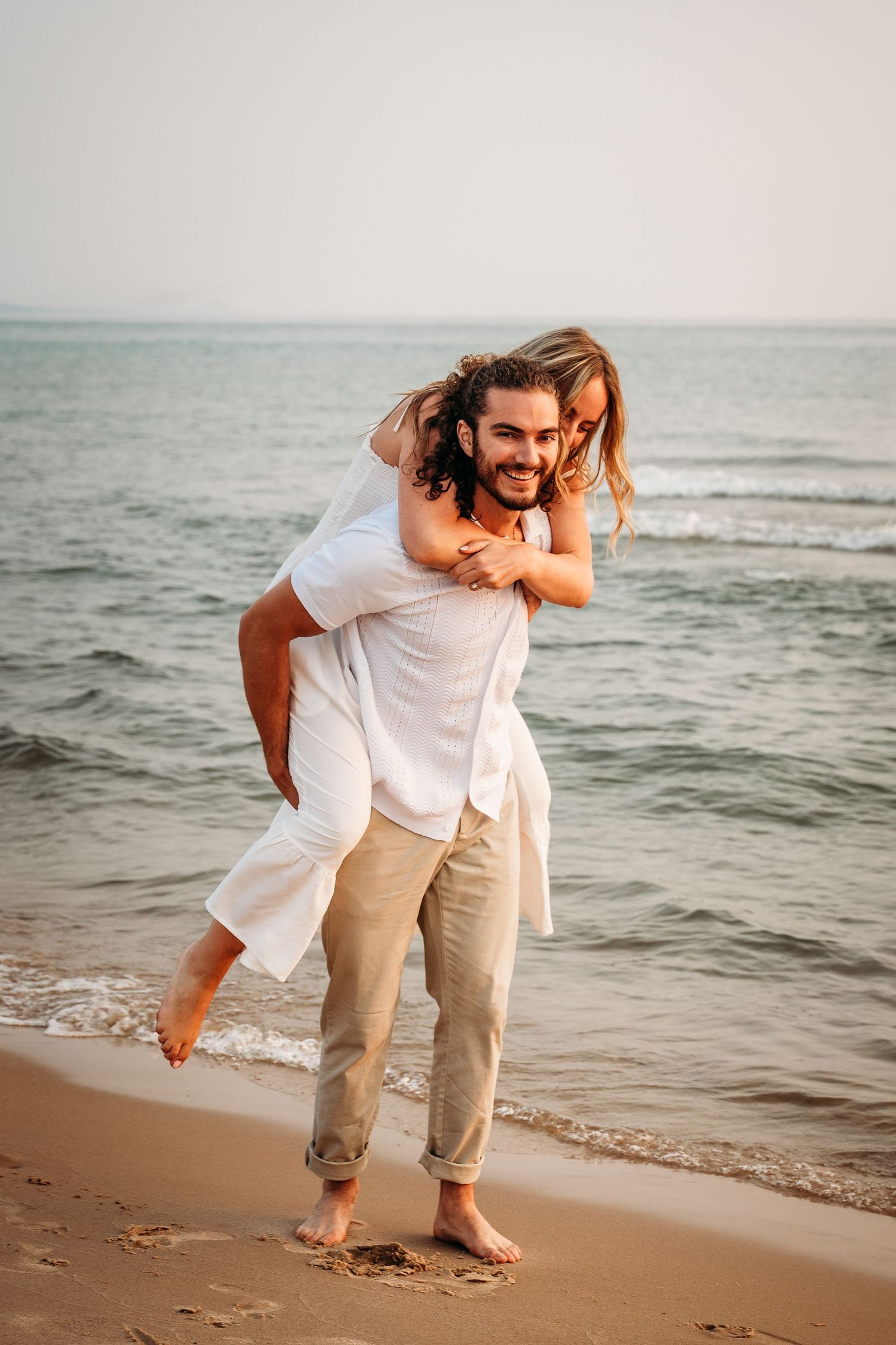 A playful piggyback ride on the beach with ocean waves in the background.