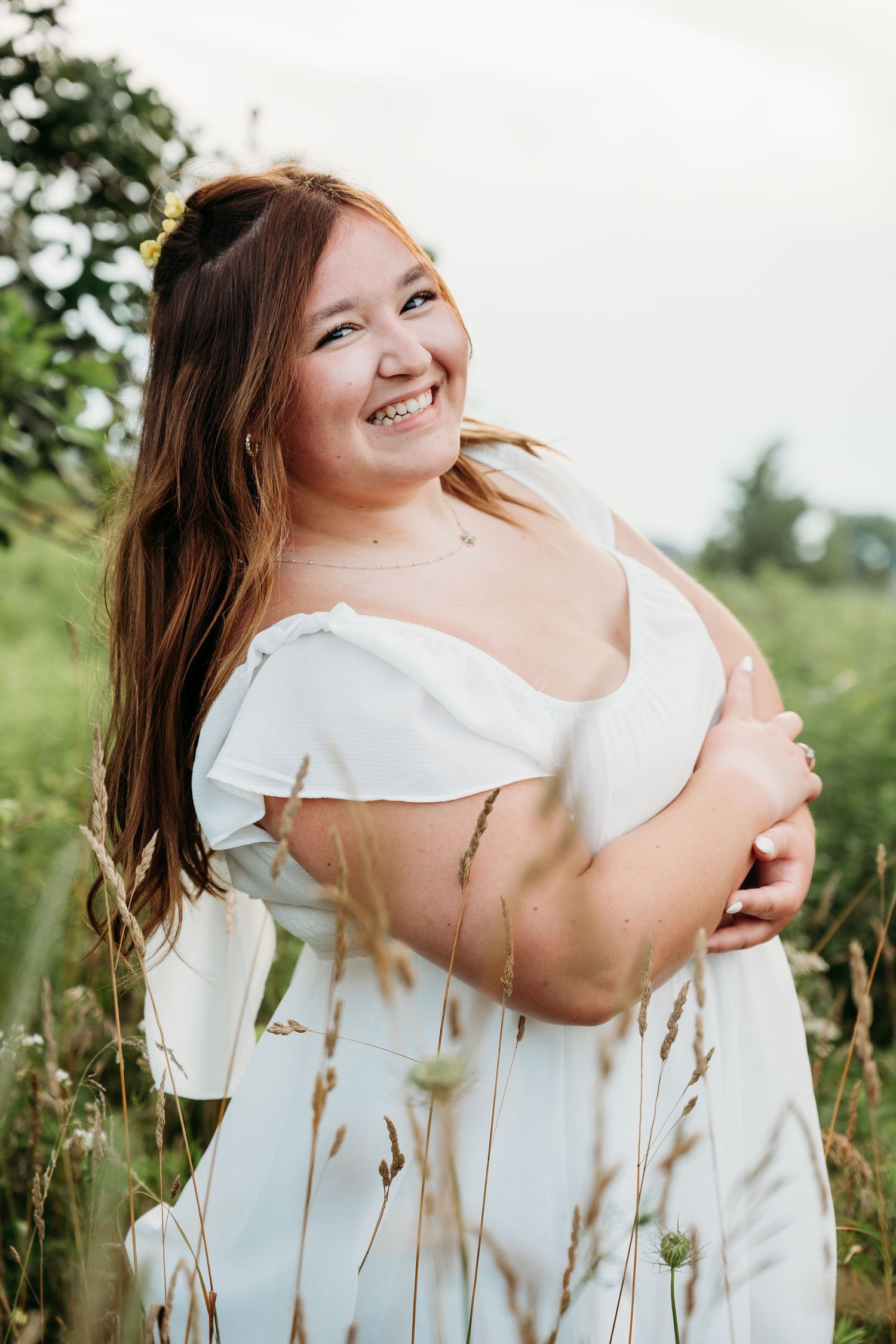 A joyful portrait in a white dress amidst tall summer grass and natural sunlight.